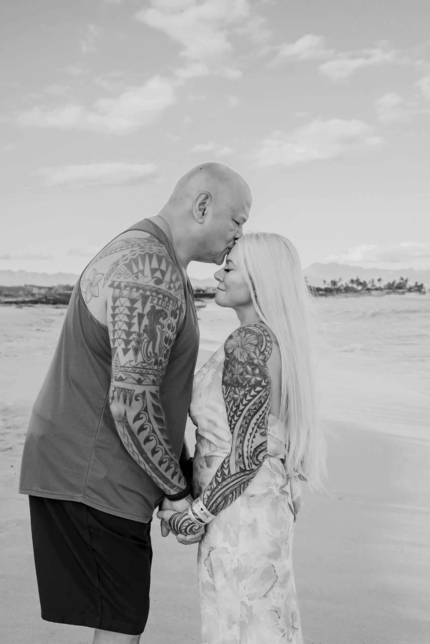 A couple embraces on a beach with the ocean and cloudy sky in the background, shown in a series of black and white photos.