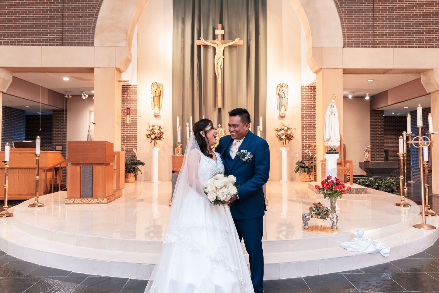 Bride and groom share a romantic moment at a church altar with a crucifix and candles in the background.