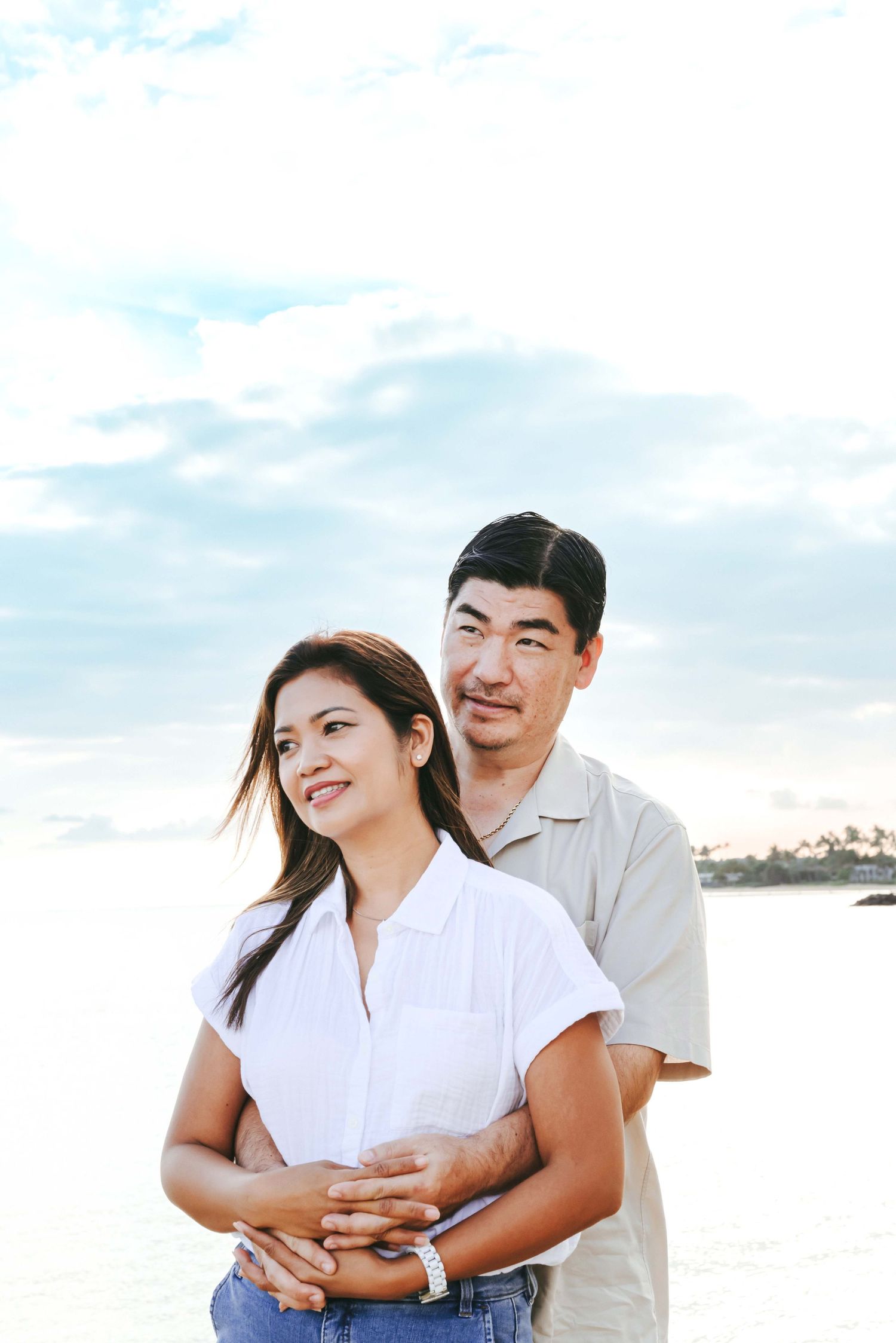 A couple in white shirts share a joyful moment together outdoors against a bright sky background.