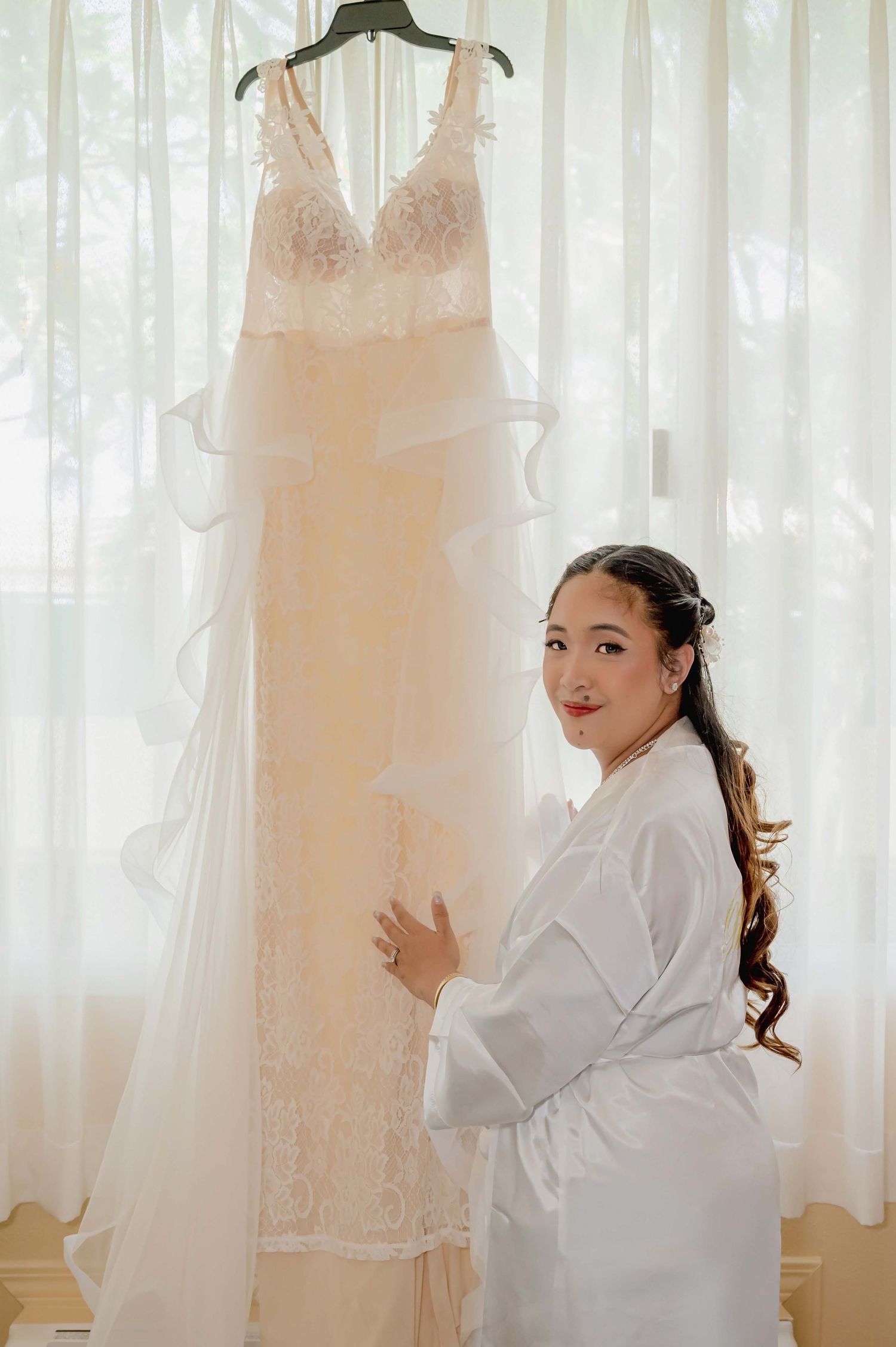 Multiple wedding dresses hang on display while someone in a white robe poses between them in a bridal boutique.