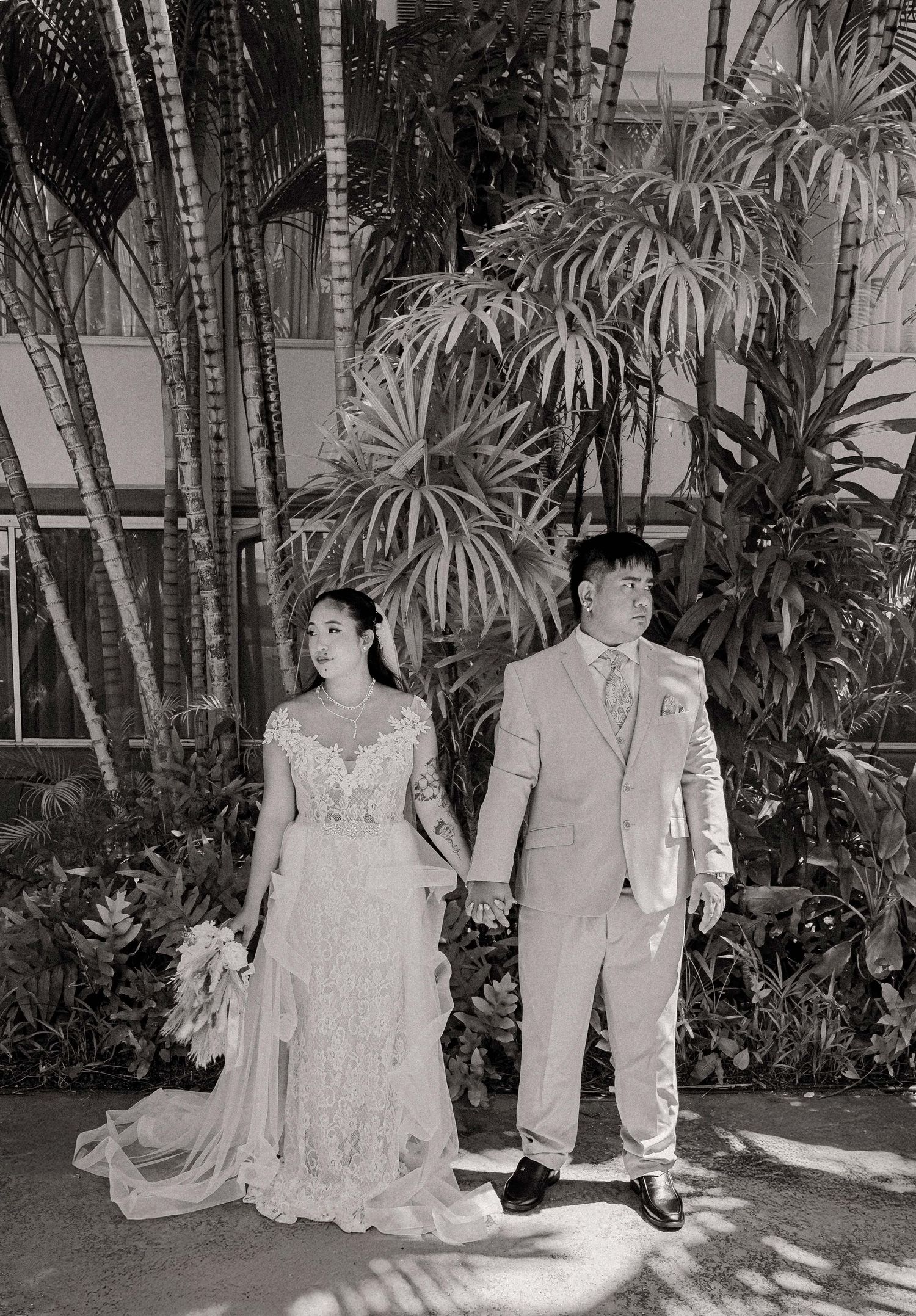 A vintage wedding photo shows a couple in lace dress and light suit standing among tropical palm trees.