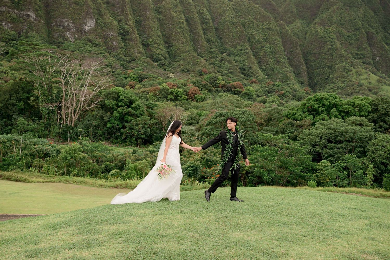 A couple poses against a backdrop of lush green mountains during their wedding photo session in Hawaii.