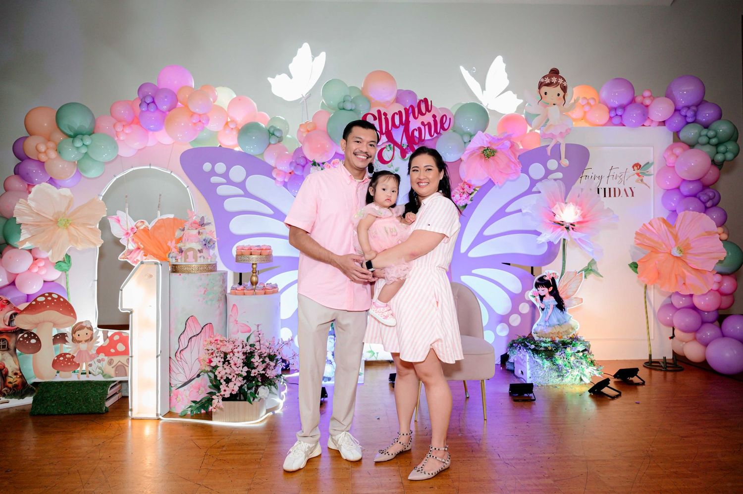 Family posing in front of a colorful butterfly-themed birthday party backdrop with balloon arch decorations.