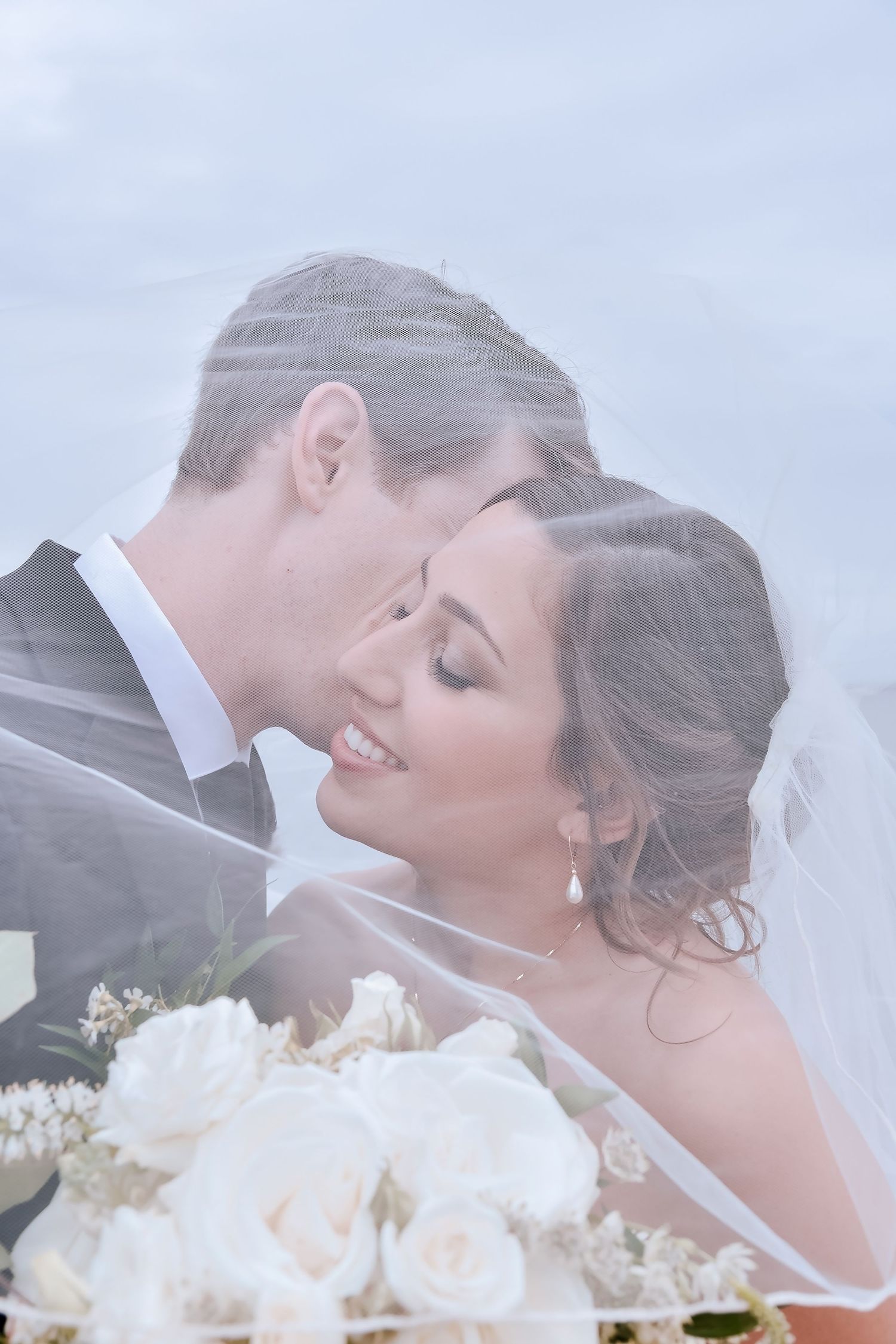 Close intimate moment between newlyweds with white roses and bridal veil in a dreamy soft-focus shot.