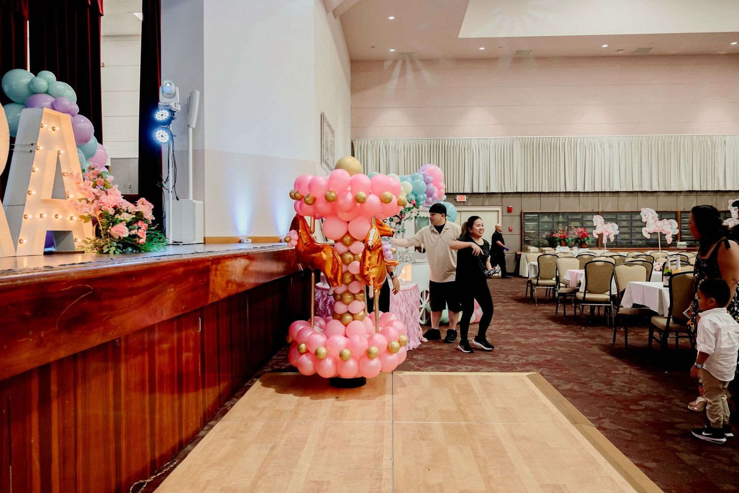 Colorful balloon decorations and floral arrangements in a banquet hall setup for a festive celebration event.