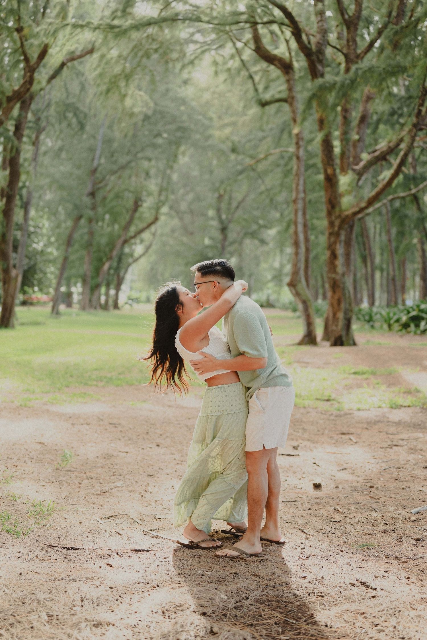 A romantic couple embraces and dips in a dreamy forest setting with dappled sunlight filtering through the trees.