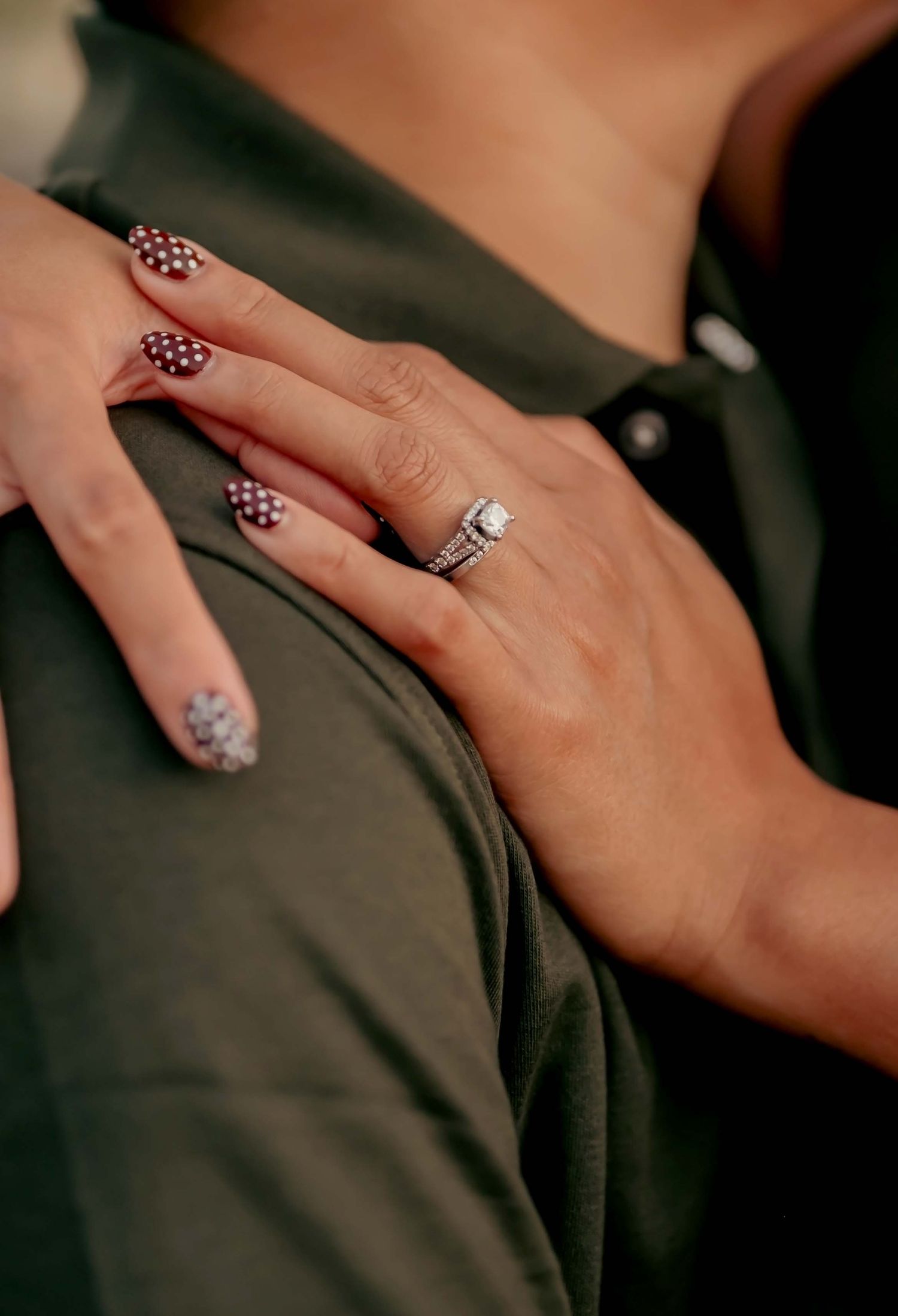 A hand wearing a silver ring is shown against a dark background with polka dot nail art designs.