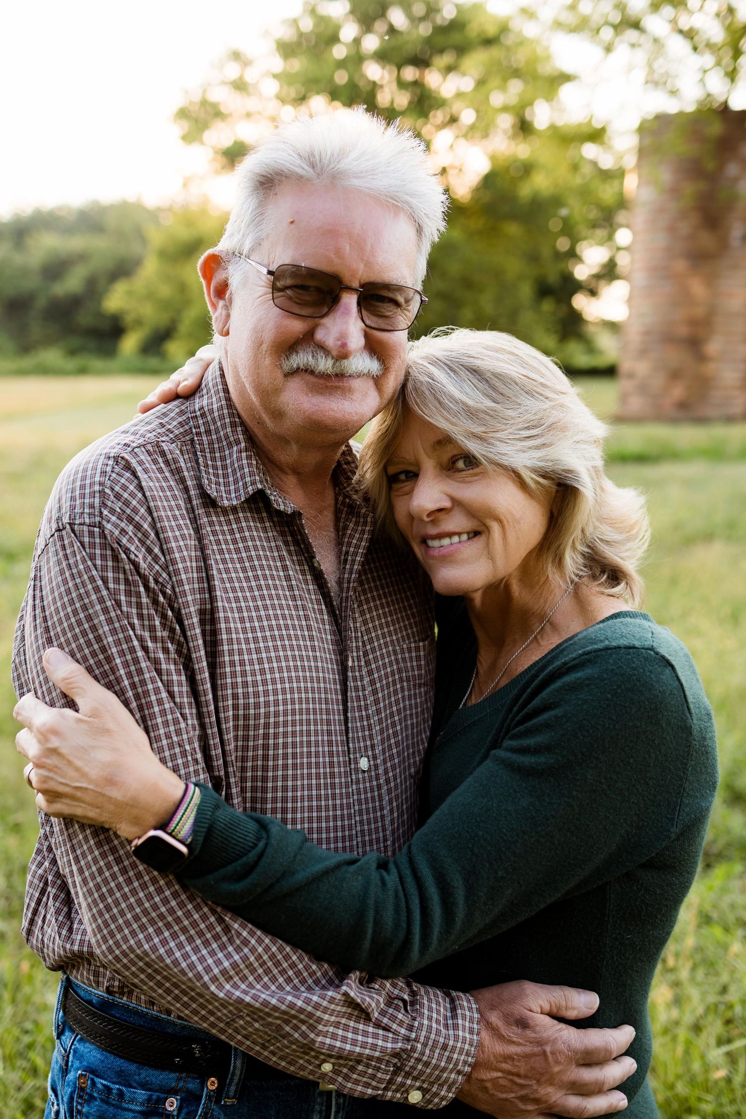 A loving senior couple embraces outdoors in a natural setting during golden hour.