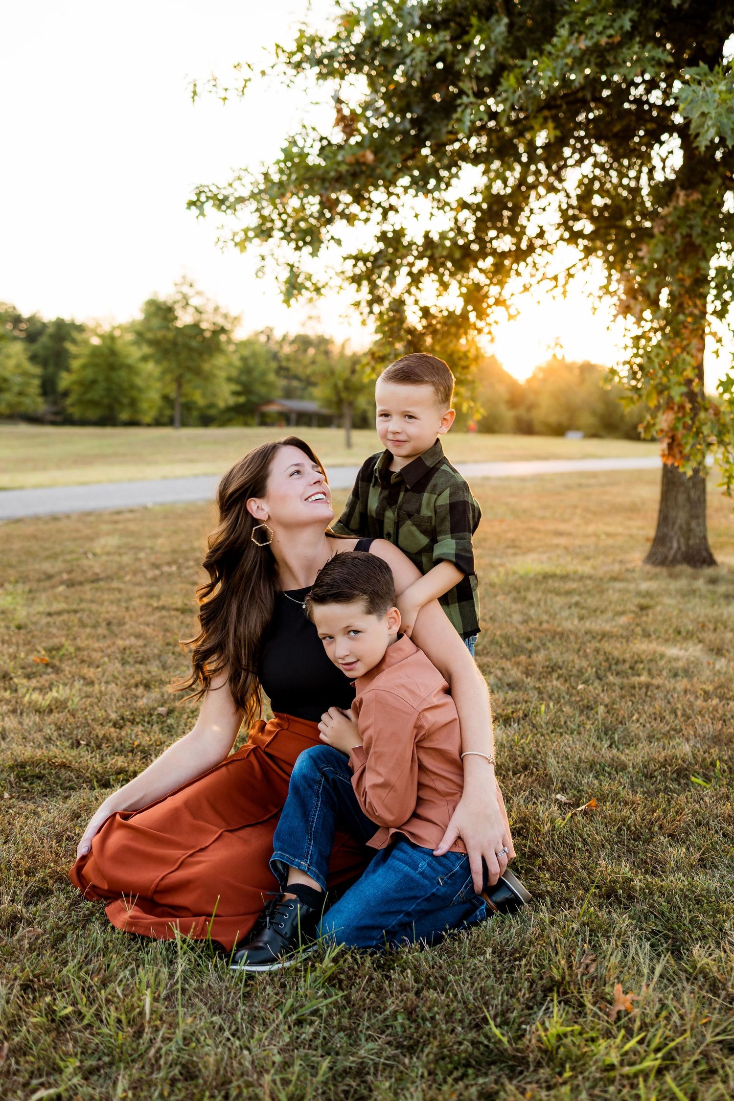 A family sits together on grassy field at sunset sharing tender moments under trees in warm autumn light.