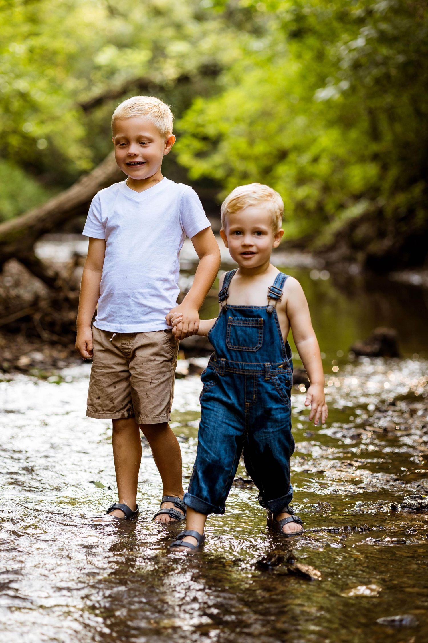 Two small children splash and play together in a shallow creek on a sunny summer day.
