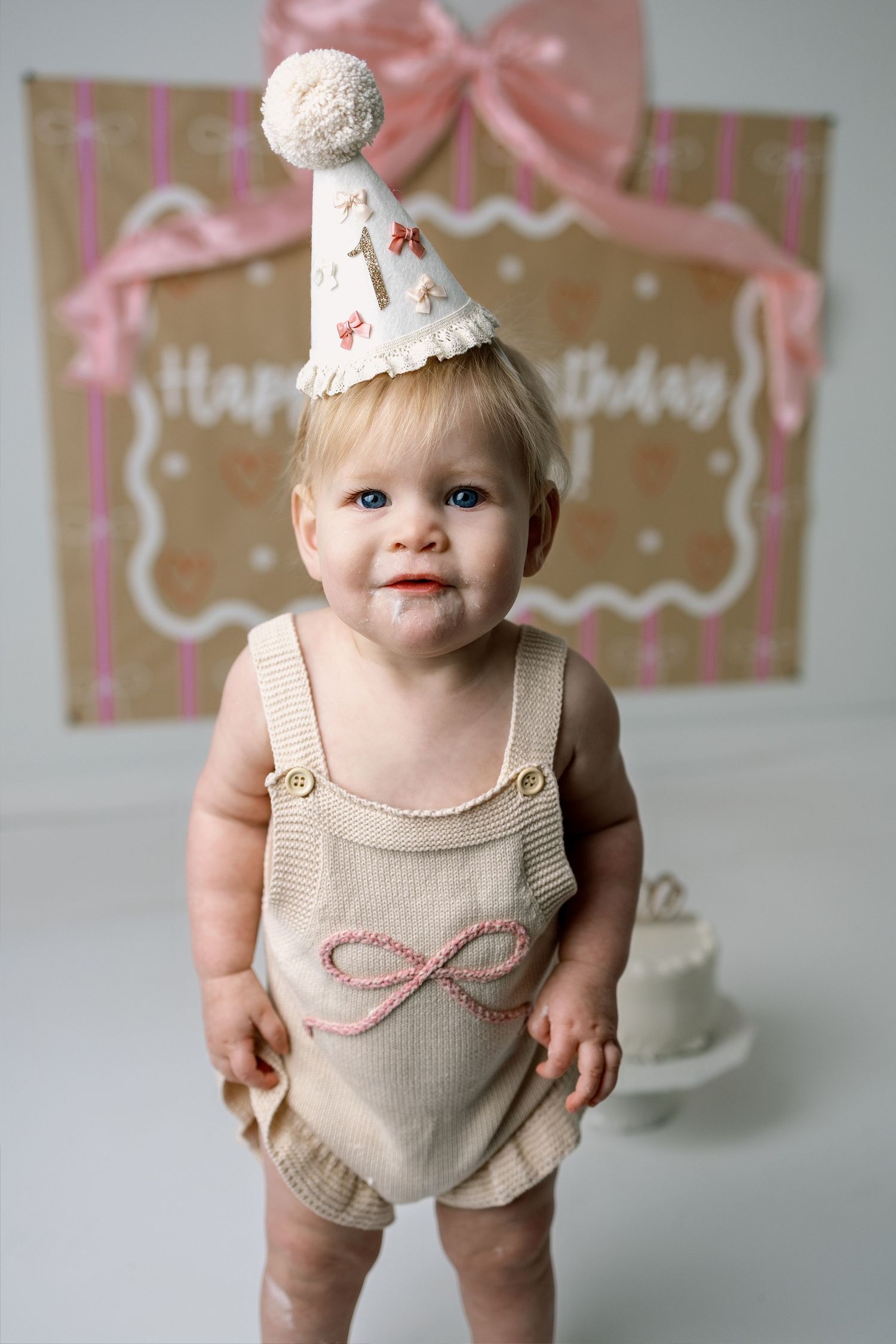 Birthday photo setup featuring beige romper outfit and pink bow decorations.