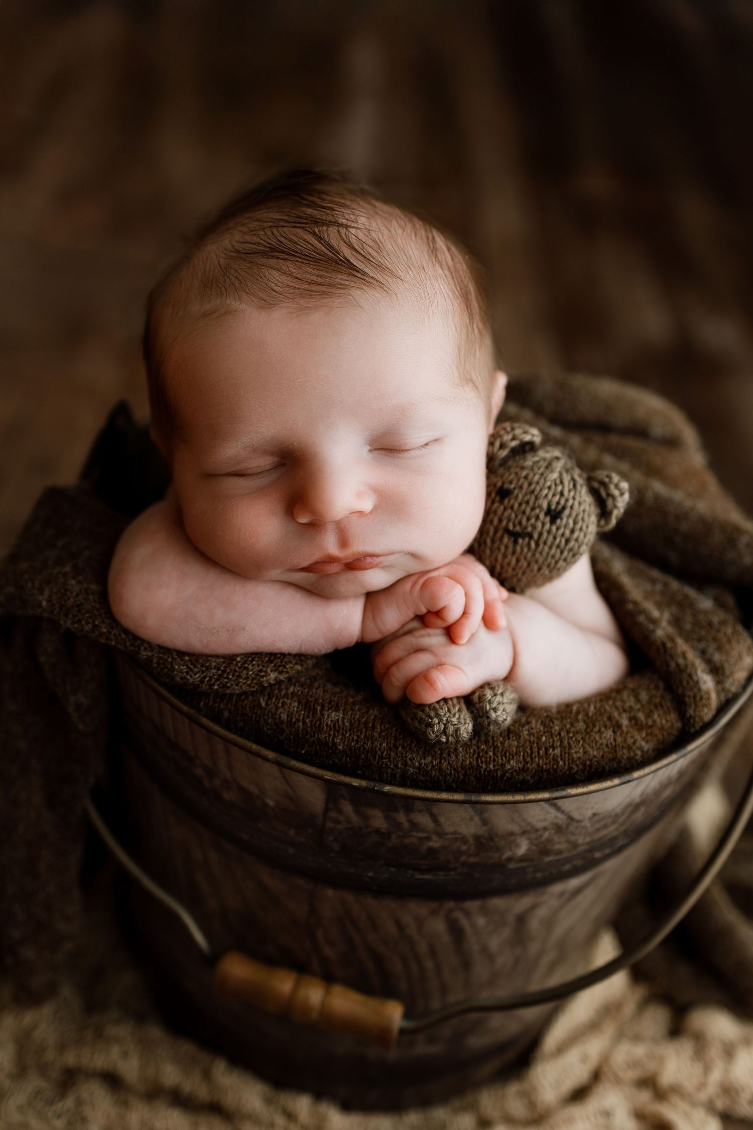 Sleeping newborn posed with a teddy bear in a rustic wooden bucket during an Edwardsville newborn photography session