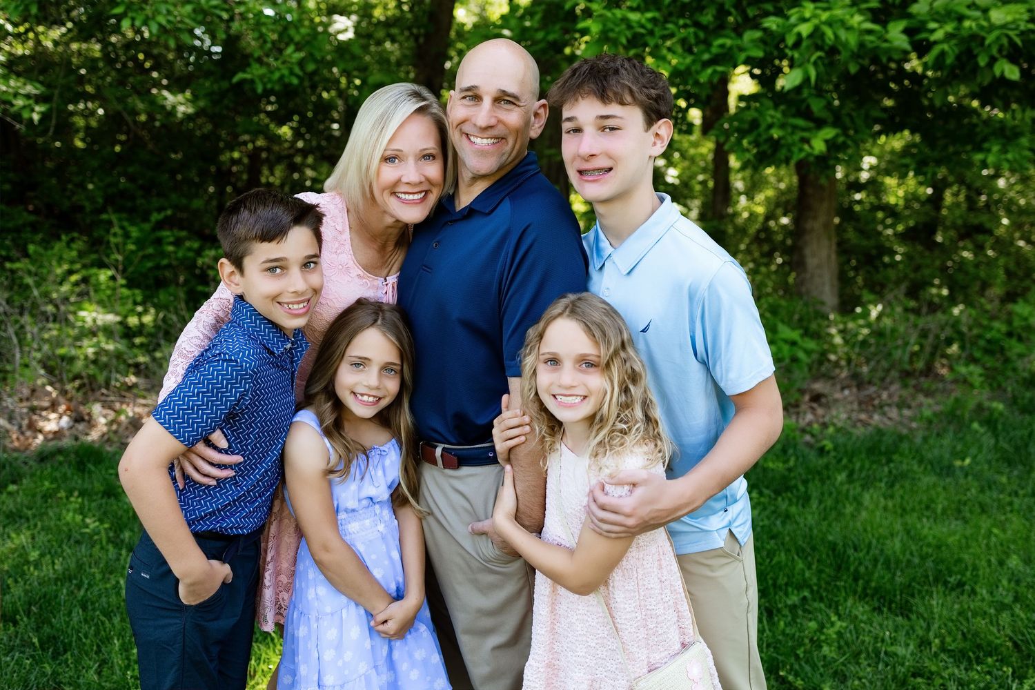 Family of six smiling together in coordinated outfits during an outdoor family photography session near Edwardsville