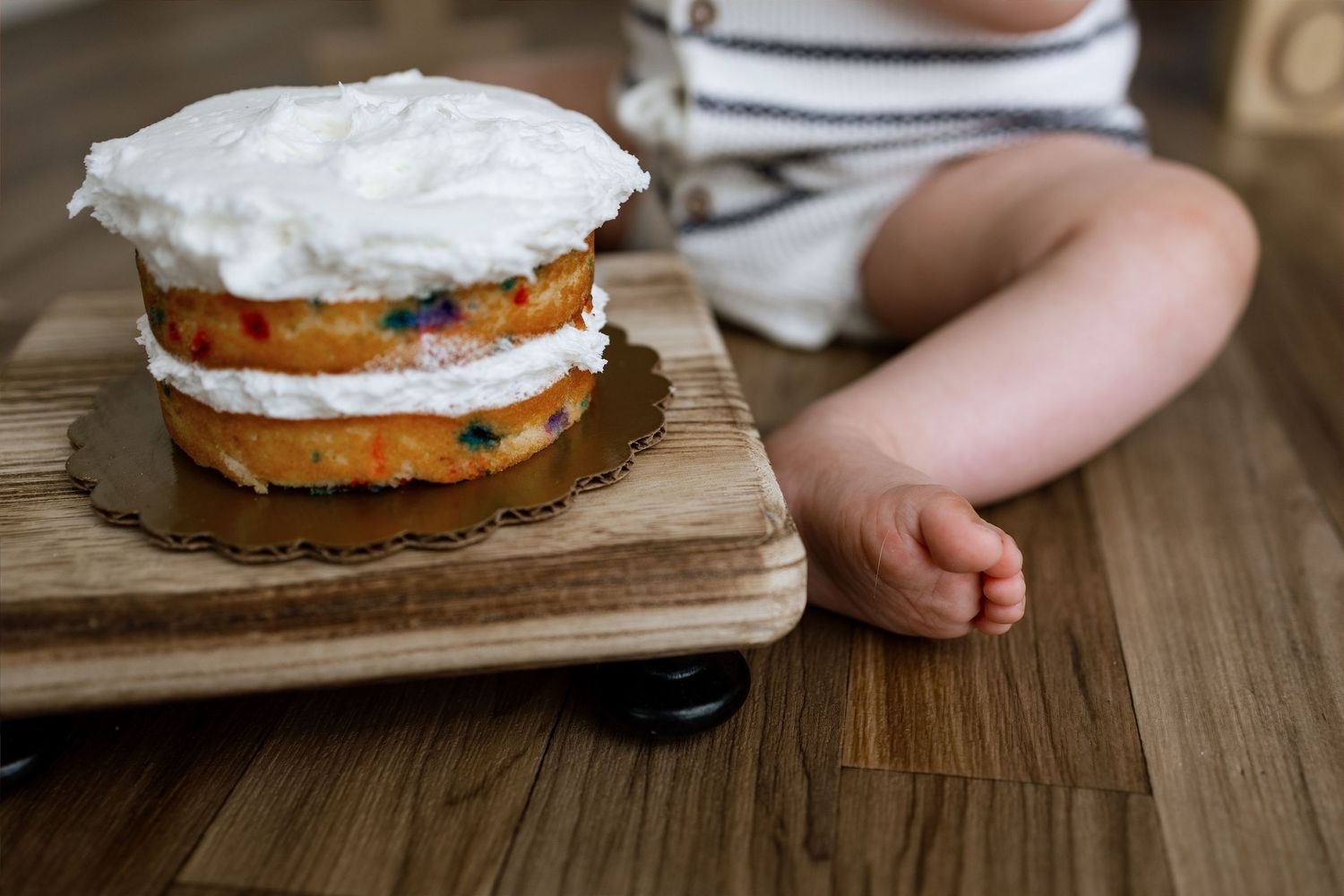 Close-up of a baby beside a colorful first-birthday smash cake during a studio milestone session