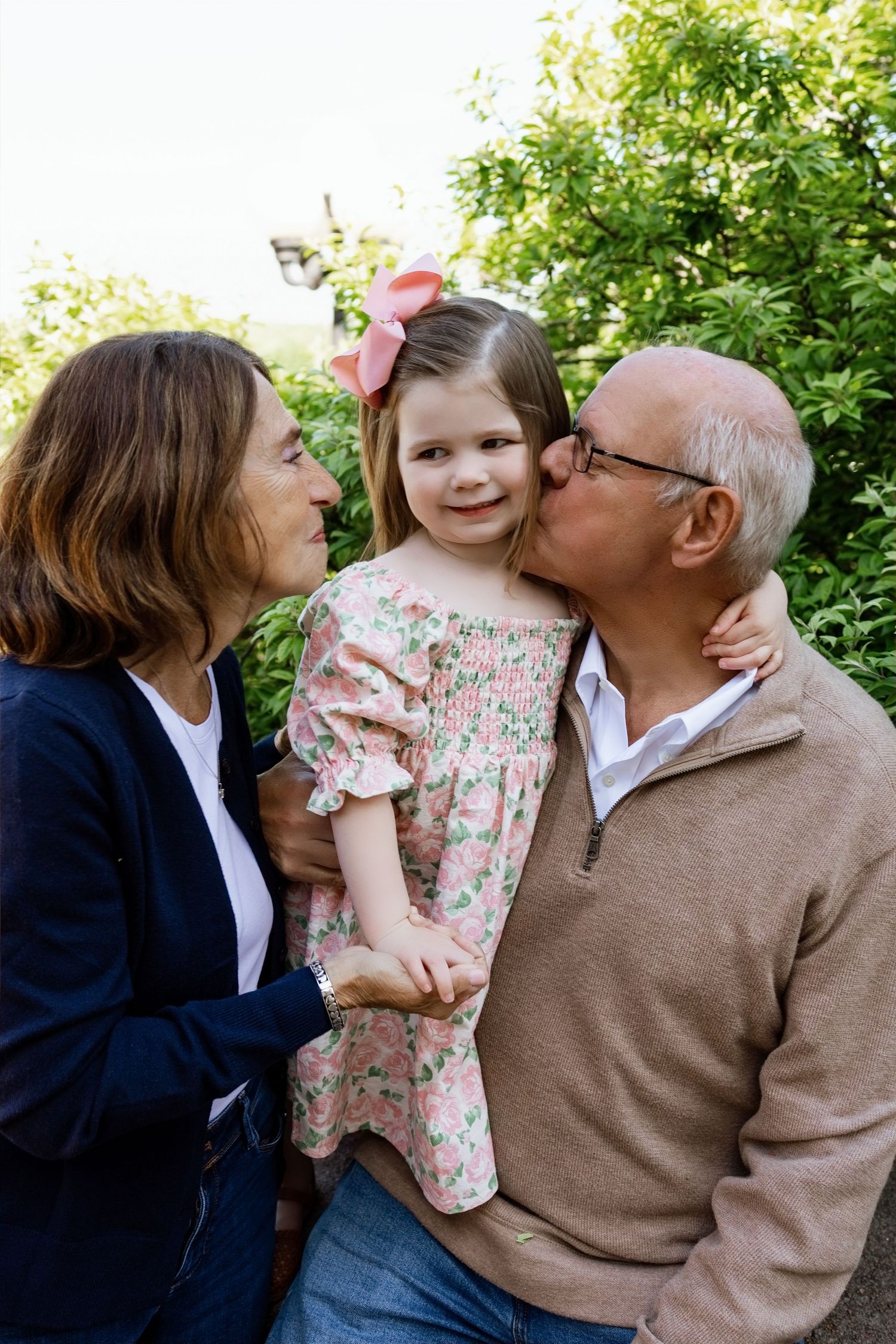 Grandparents kissing their smiling granddaughter during an outdoor multigenerational family photography session