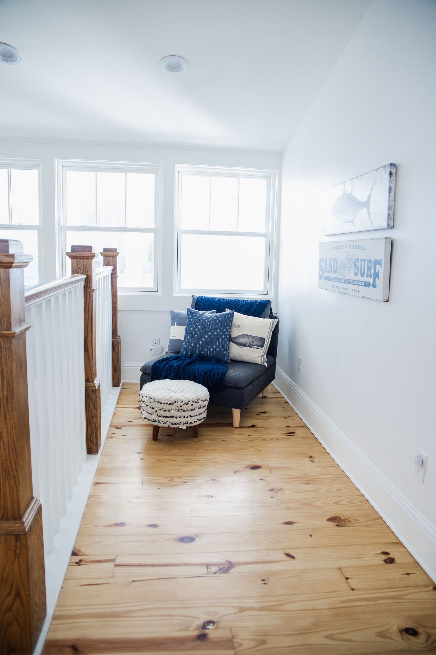 Cozy reading nook with navy blue chair and wooden floors in bright sunlit hallway with white walls.