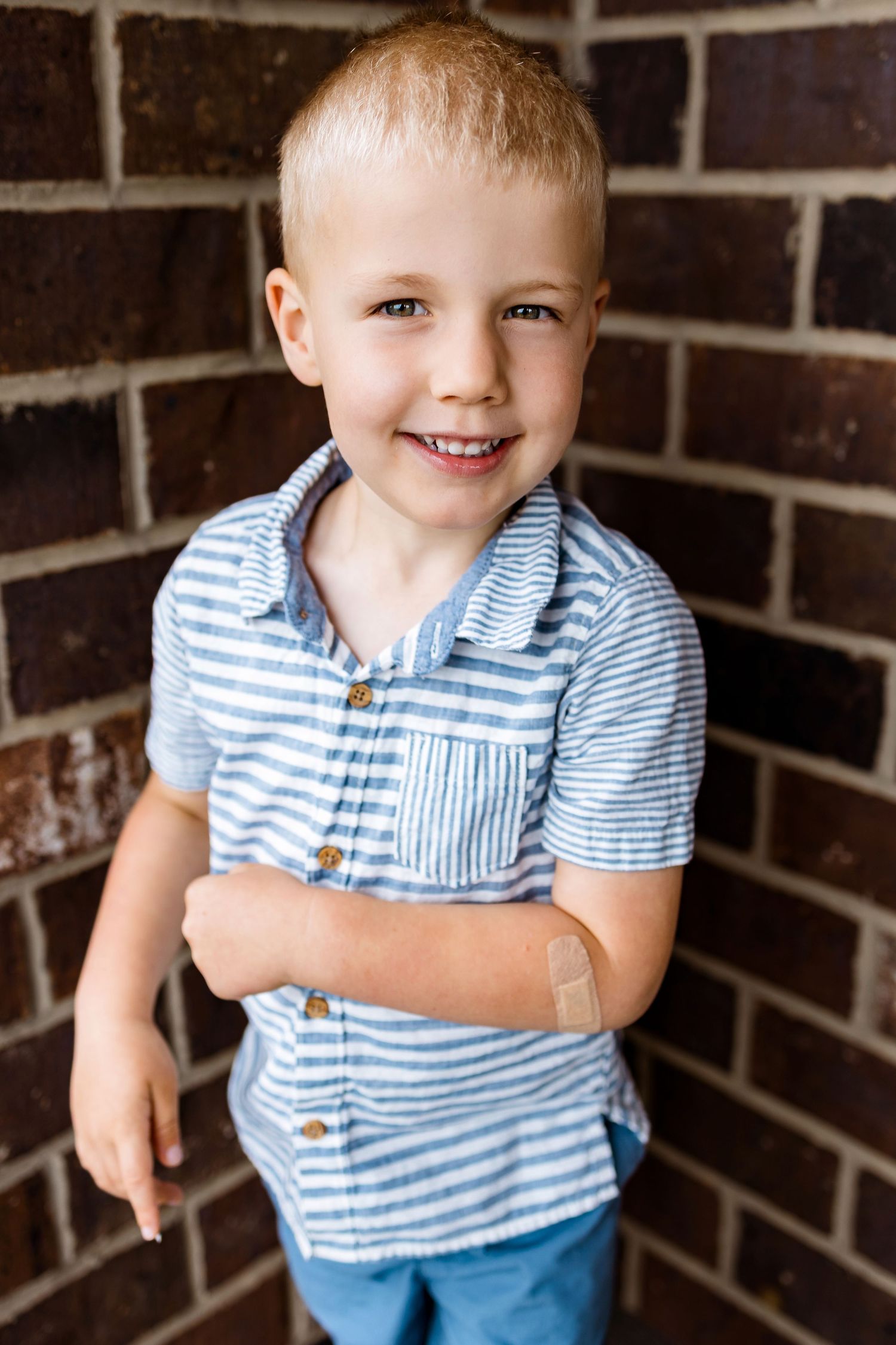 A child wearing a blue and white striped shirt smiles against a brick wall background.