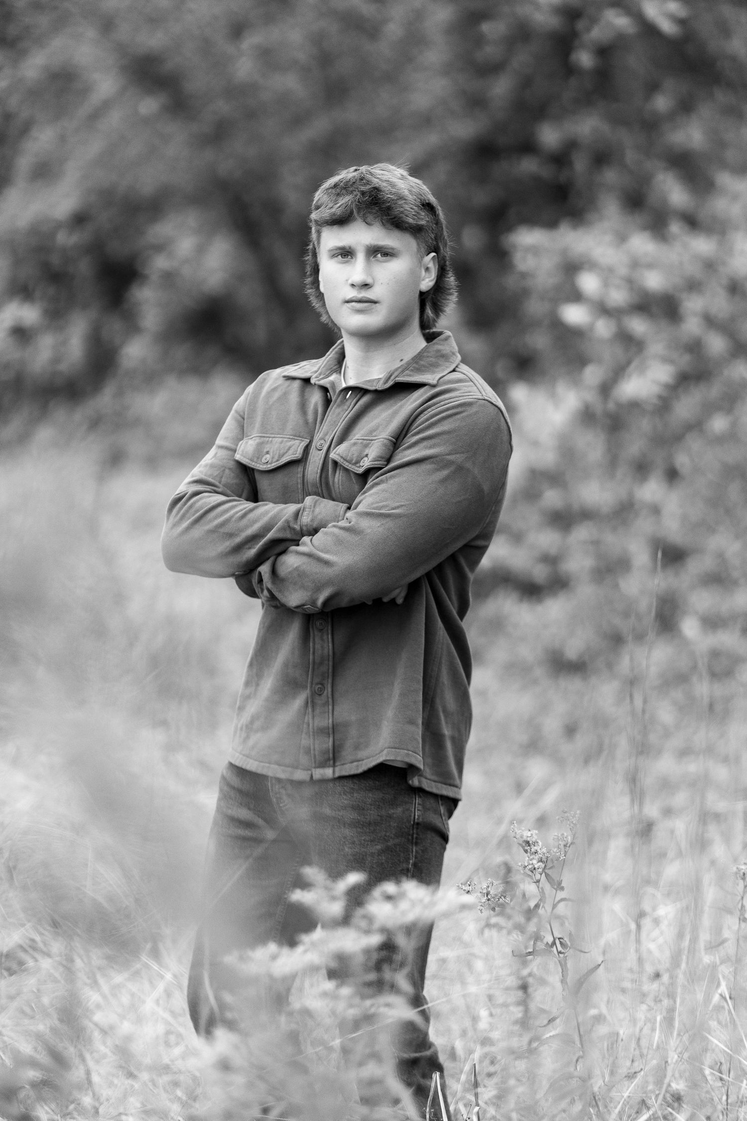 Black and white portrait of person in casual attire standing in field of tall grass.
