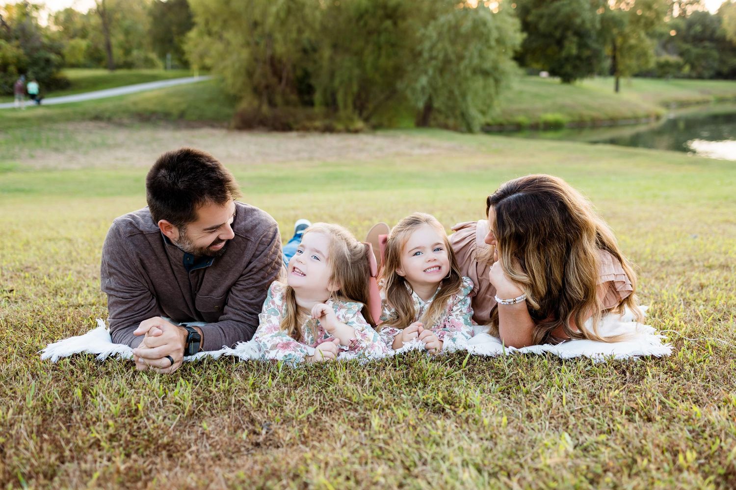 A group of people lying on grass blankets in a park setting on a sunny day.