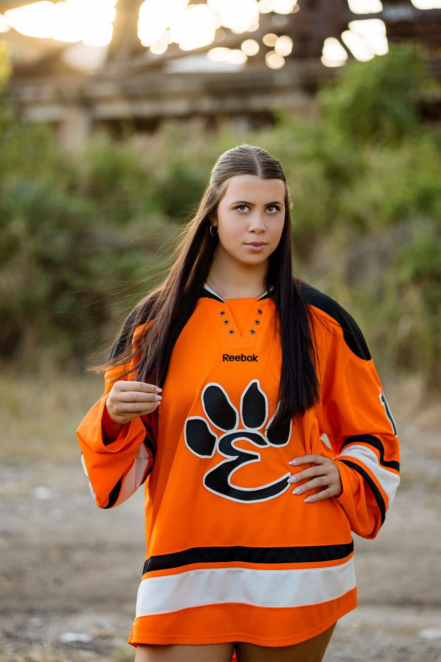 Person wearing an orange and white hockey jersey with black accents poses in an outdoor setting.