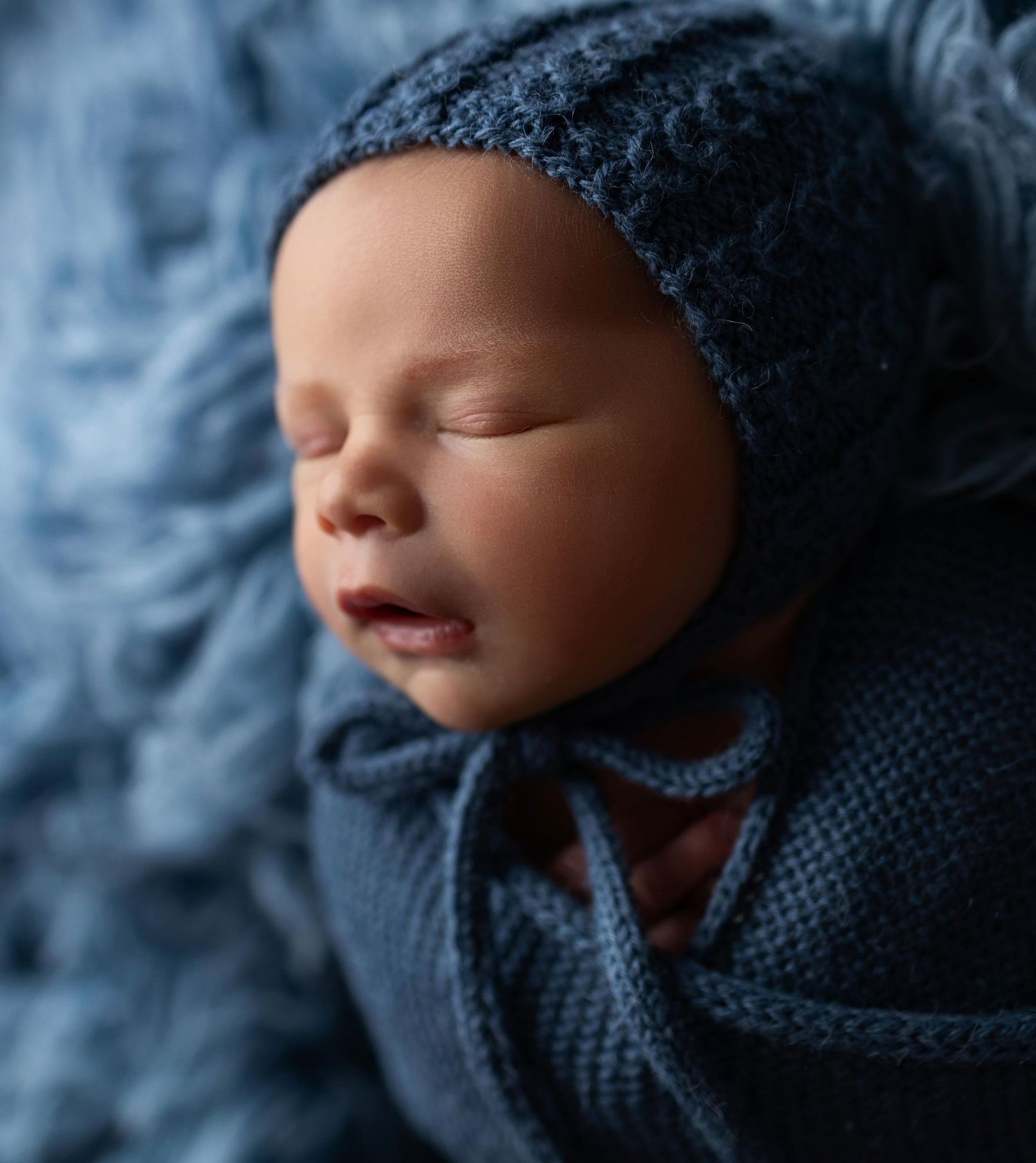 Sleeping baby wearing a gray knit hat against a dark background.
