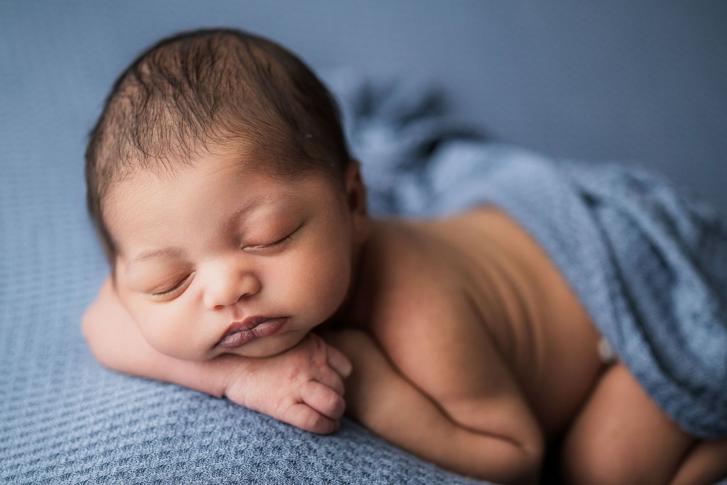 Sleeping newborn baby lies peacefully on blue textured blanket with soft denim wrap.