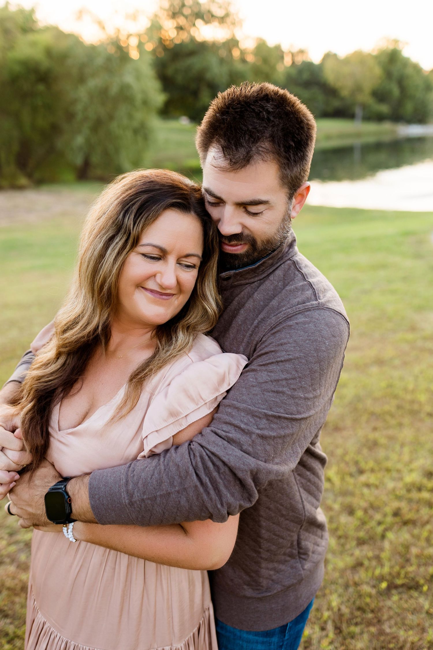 A couple shares an intimate embrace on a grassy hillside during sunset.