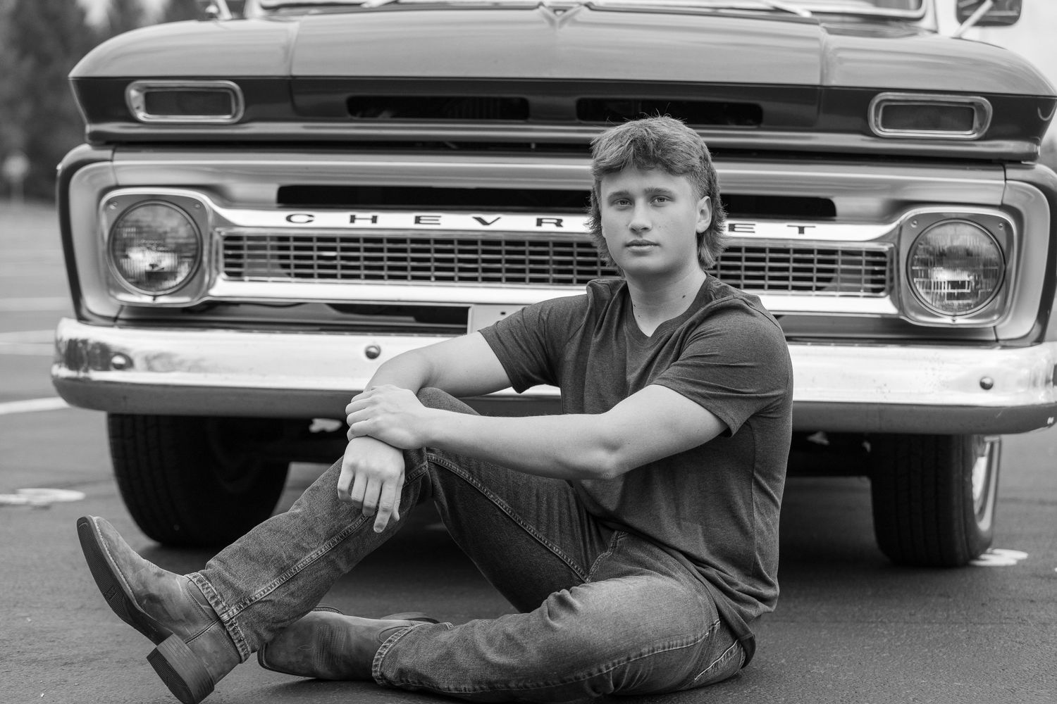 Person seated in front of vintage Chevrolet truck in black and white photo.