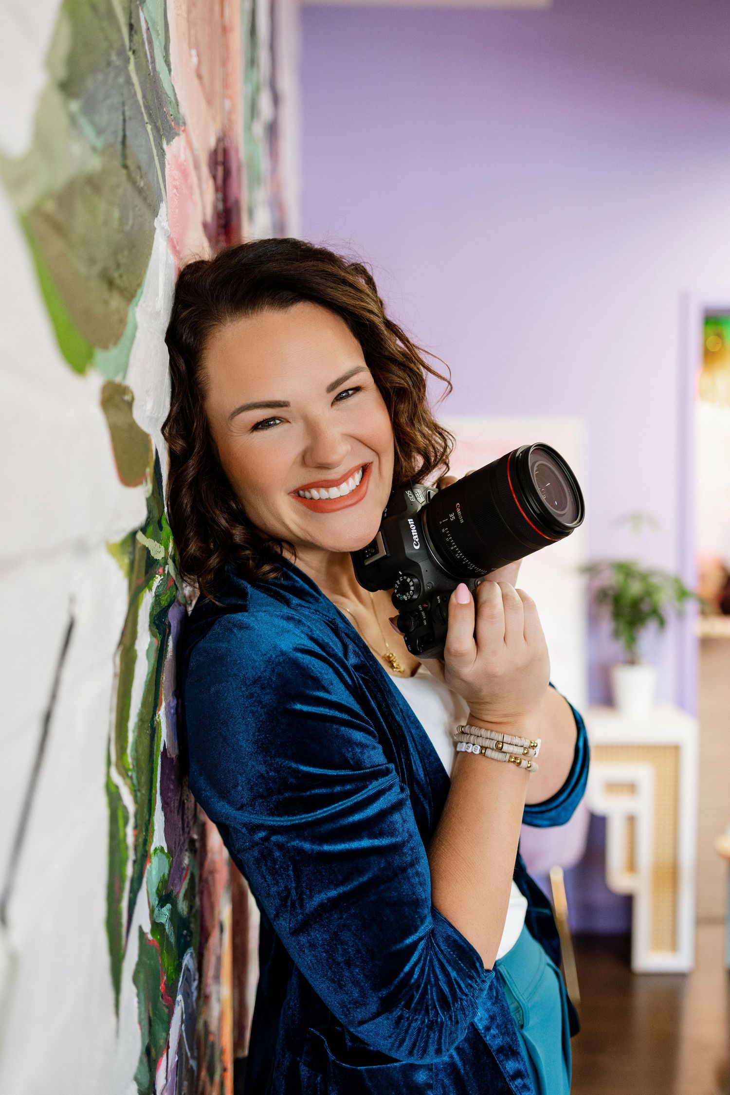 Professional photographer in navy blue blazer smiles while holding DSLR camera in bright indoor setting.