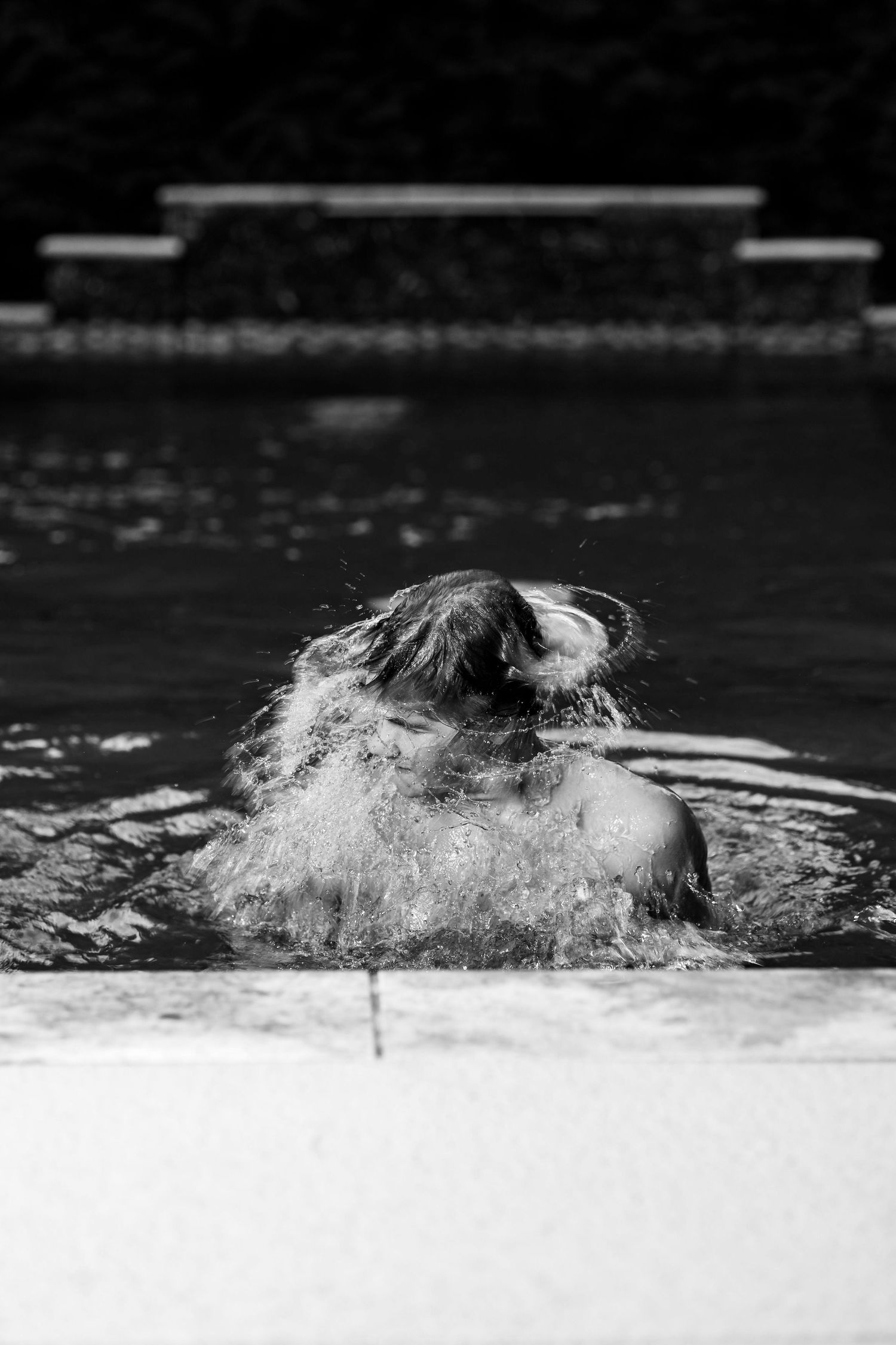 A black and white photo showing hair emerging from water in a dramatic splash at a swimming pool.