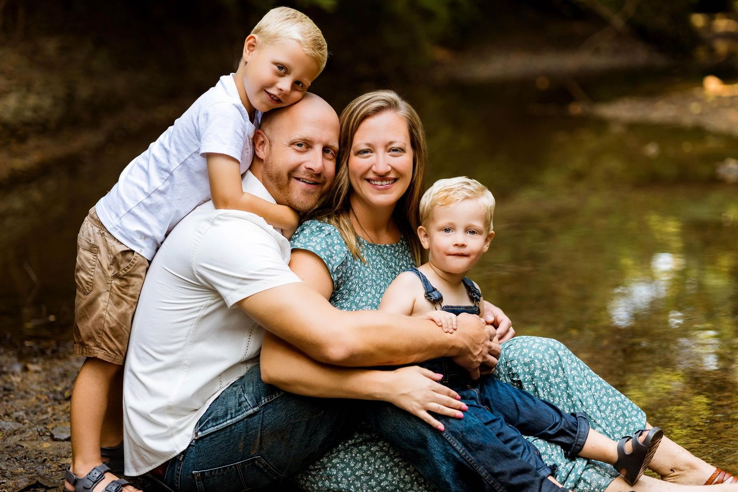 Family in casual clothing taking outdoor family portraits at a tranquil creek setting in summer.