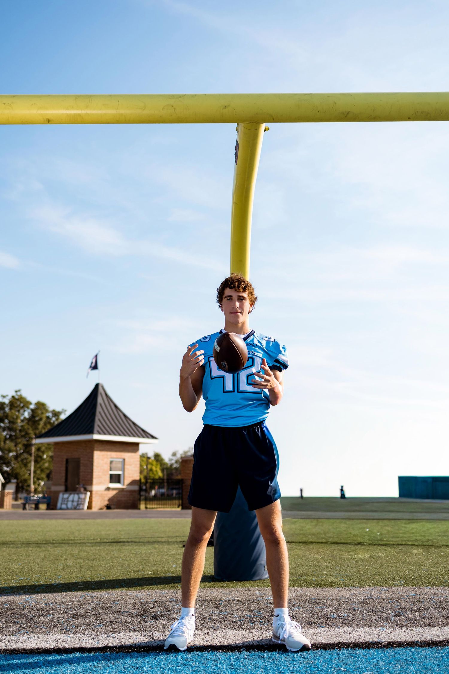 Football player in light blue jersey crouches near yellow goal post on sports field.