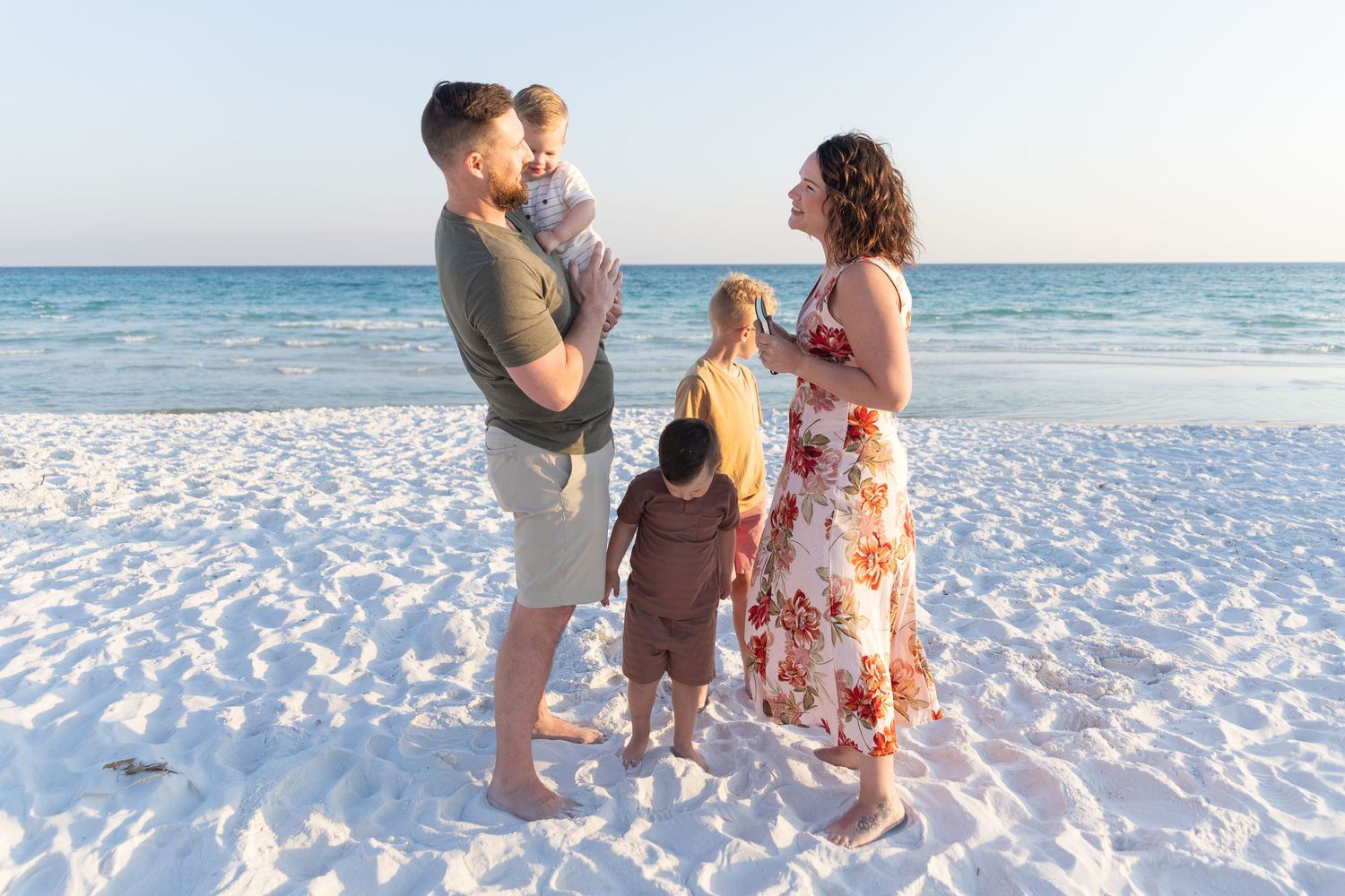 Scenic family beach portrait at sunset with turquoise ocean and white sand background.