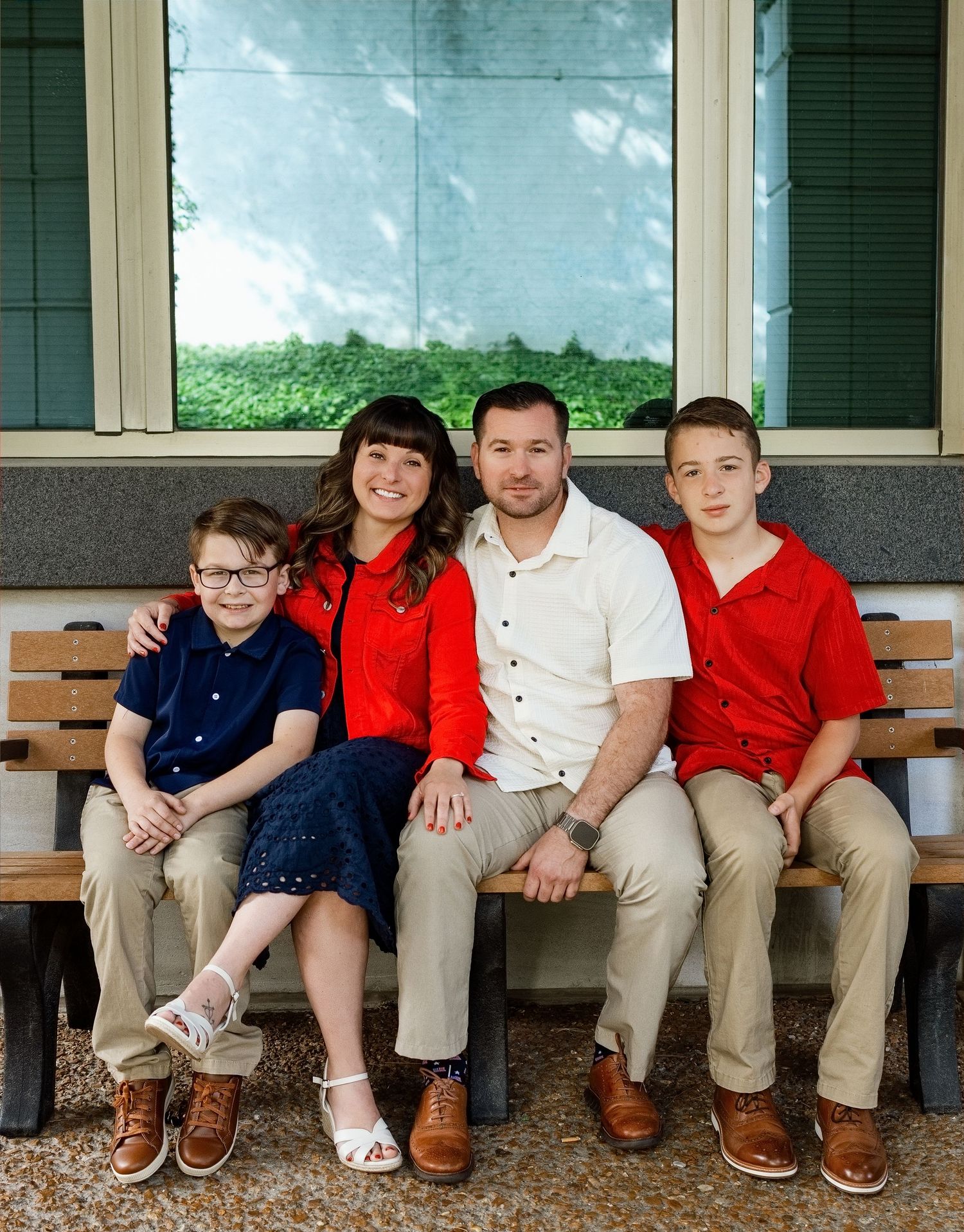 Family of four smiling together on a bench during an outdoor portrait session in the Edwardsville area