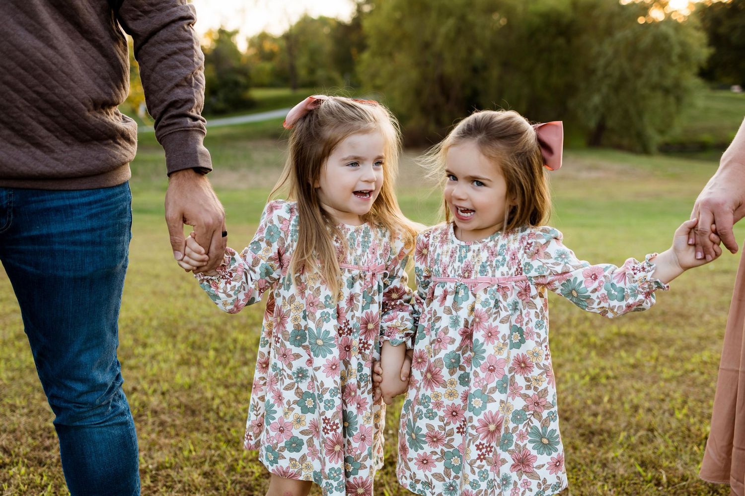 Children in floral dresses play together outdoors during golden hour in a grassy field.