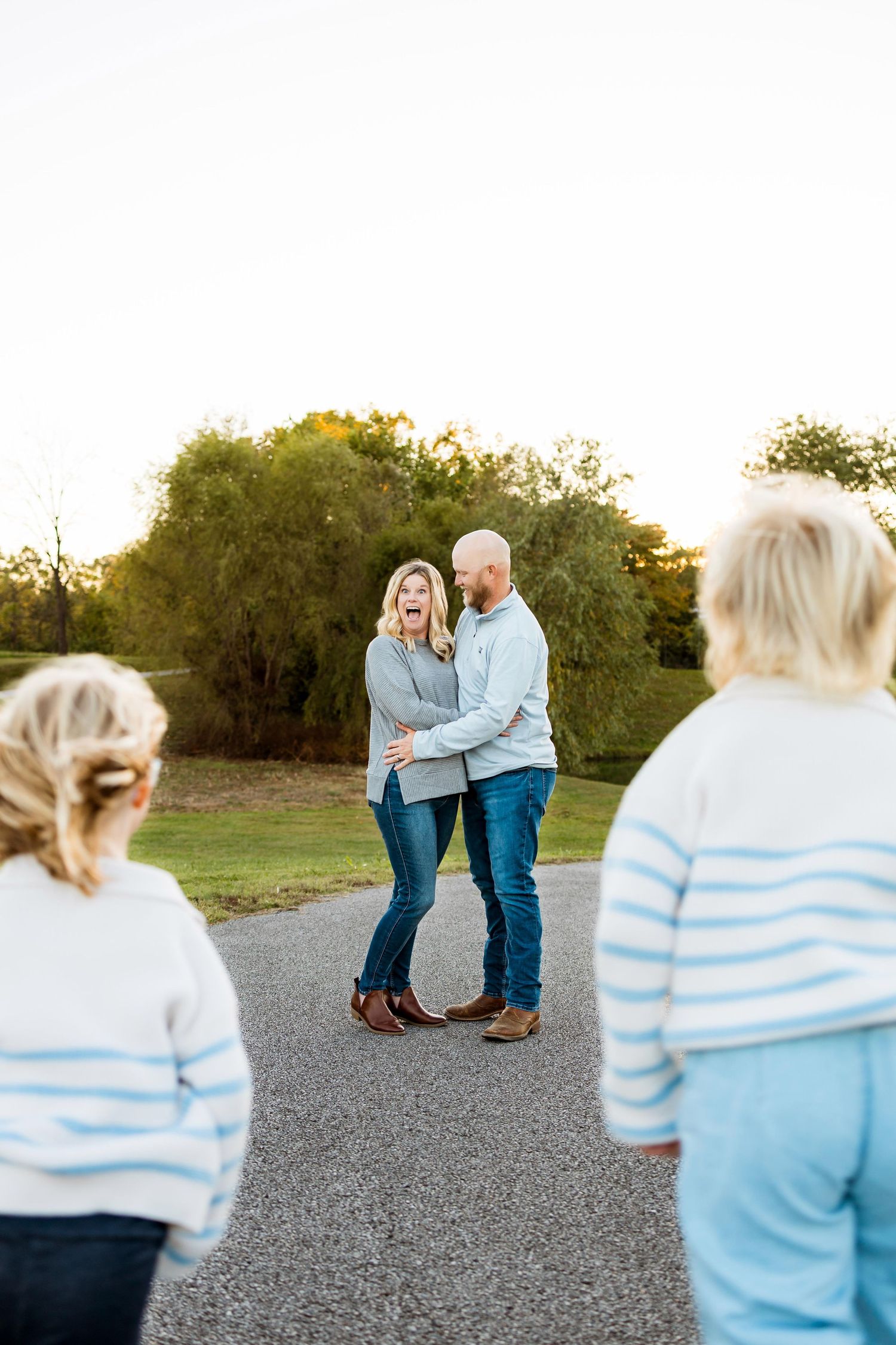 A couple embraces on a gravel path at sunset while others watch from the foreground.