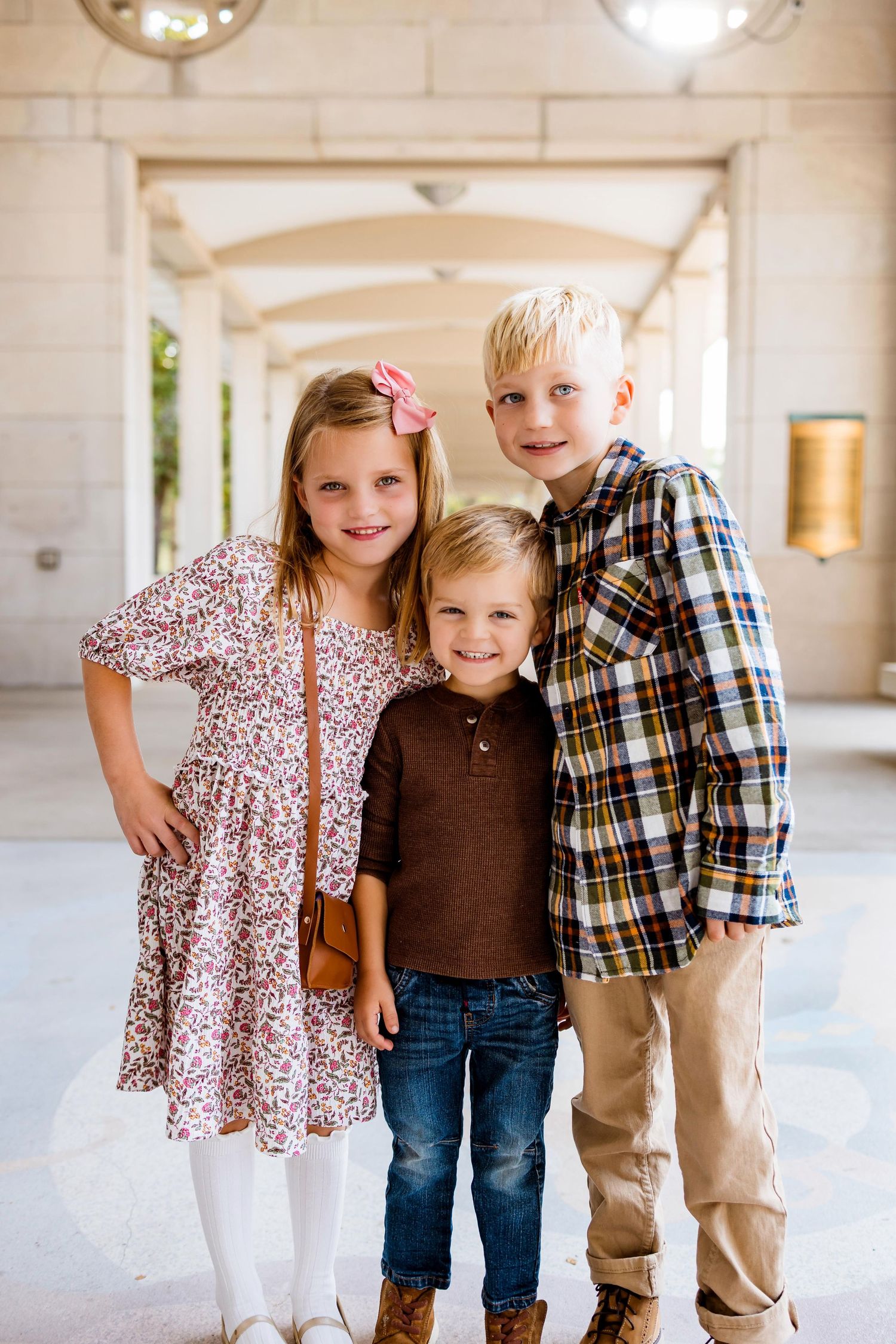 Three children stand together in a bright indoor space wearing casual clothing.