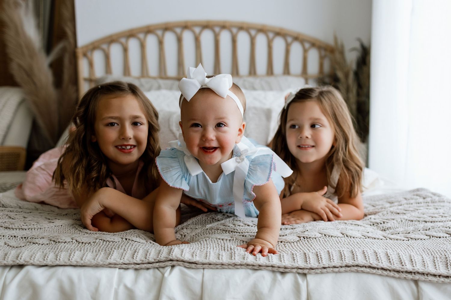 Three sisters smiling together during a baby milestone and cake smash photography session at Tara Lee Photography
