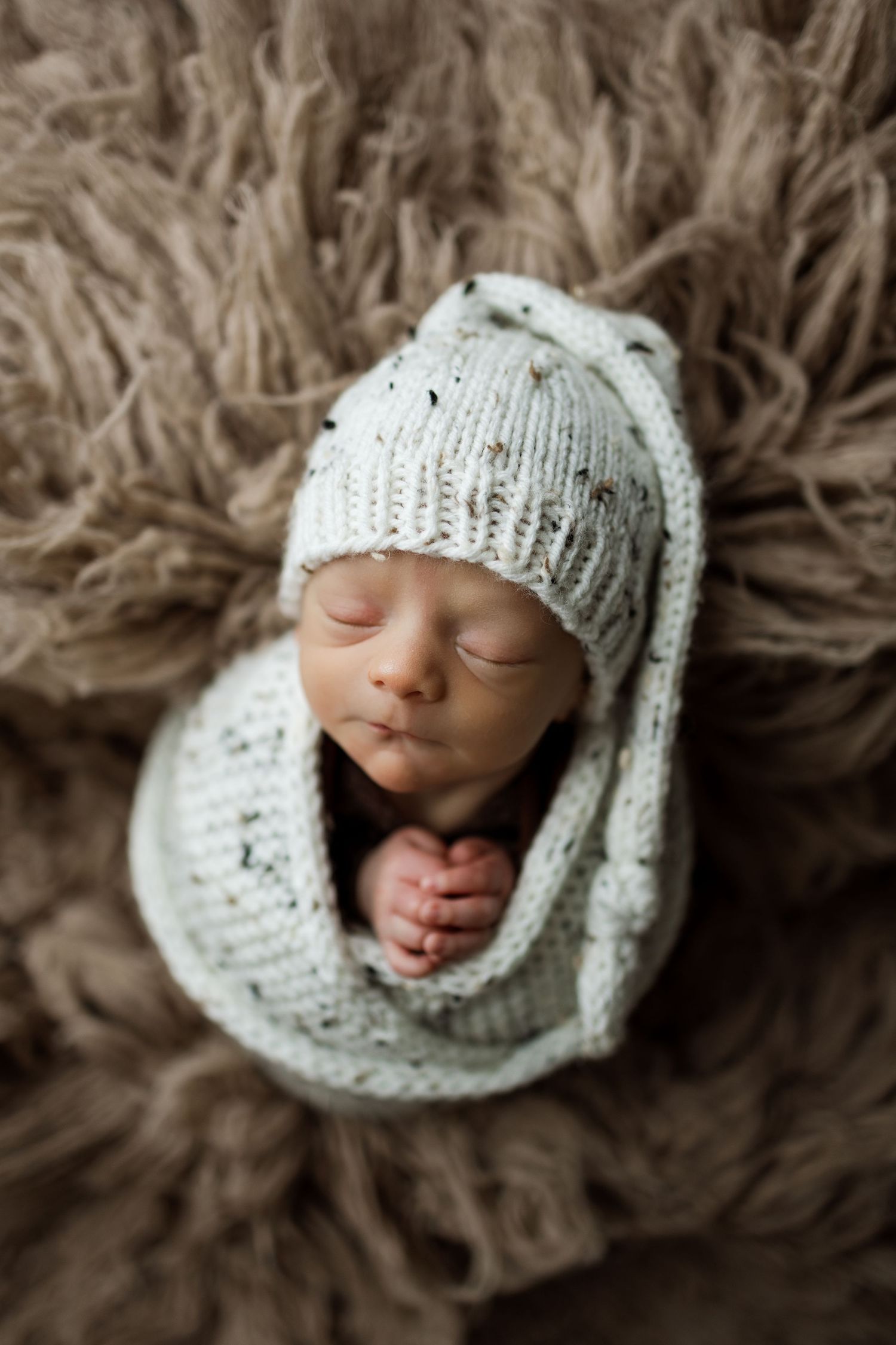 Series of newborn portraits showing tiny baby wrapped in soft knit cream-colored blanket on textured background.