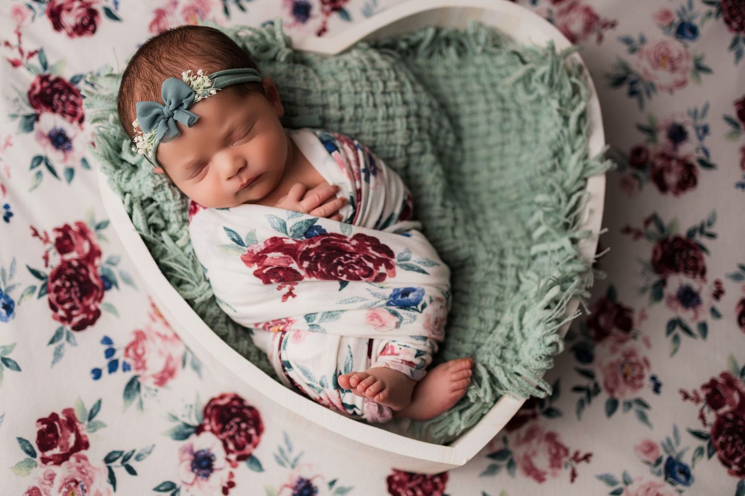 Newborn baby sleeping peacefully on floral bedding with mint green knitted blanket.