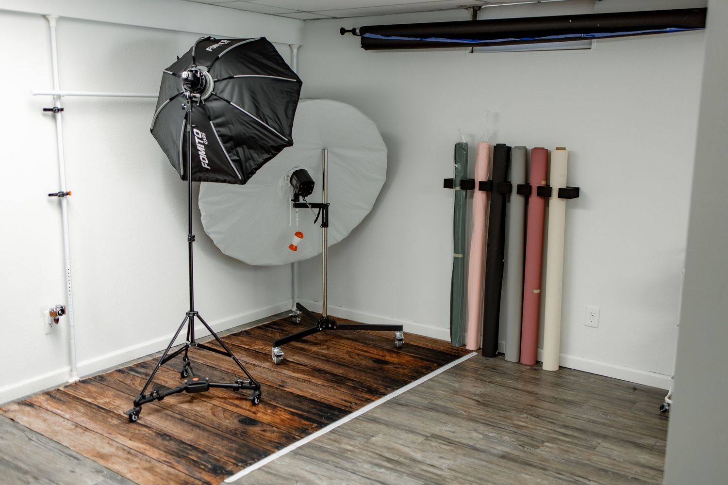 A panoramic view of a white photography studio space with wooden floors and professional lighting equipment.
