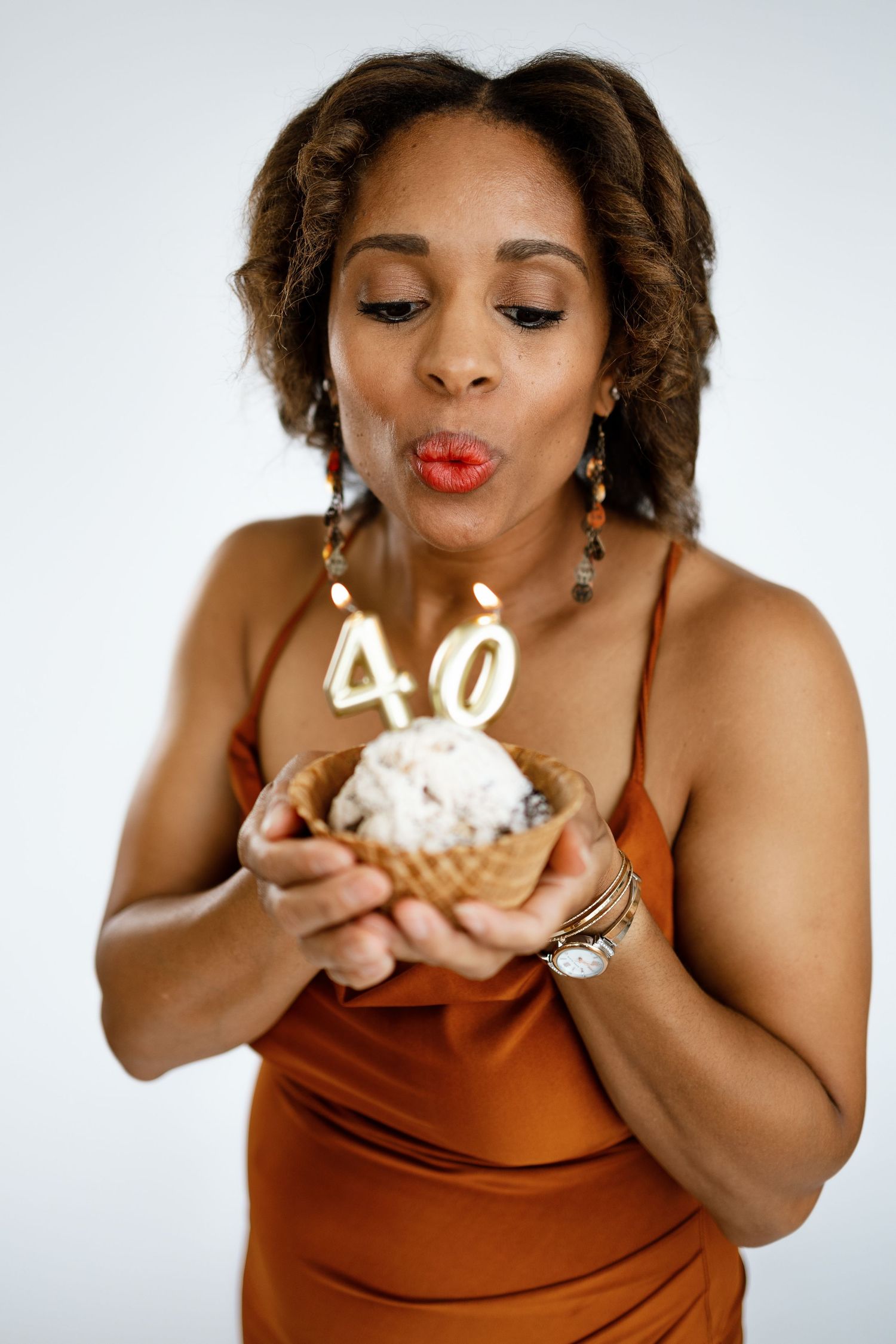 Woman in orange dress blowing out 40th birthday candles on an ice cream cone cupcake.