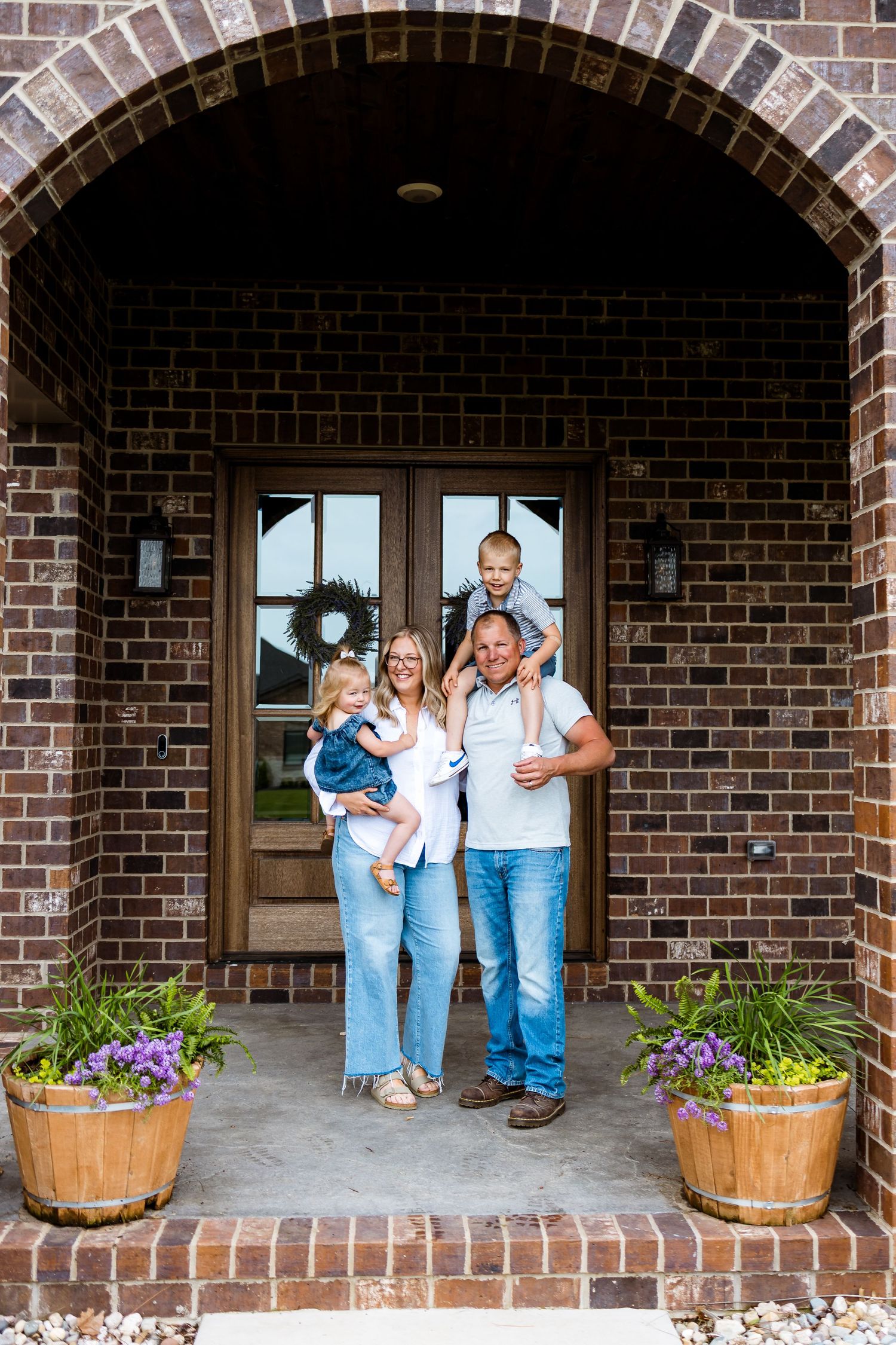 Family standing together under brick archway entrance with flower planters.