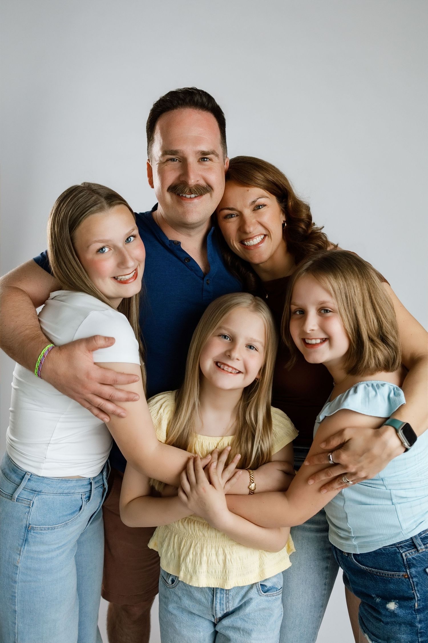 Parents hugging their three daughters during a joyful family photography session against a white studio backdrop