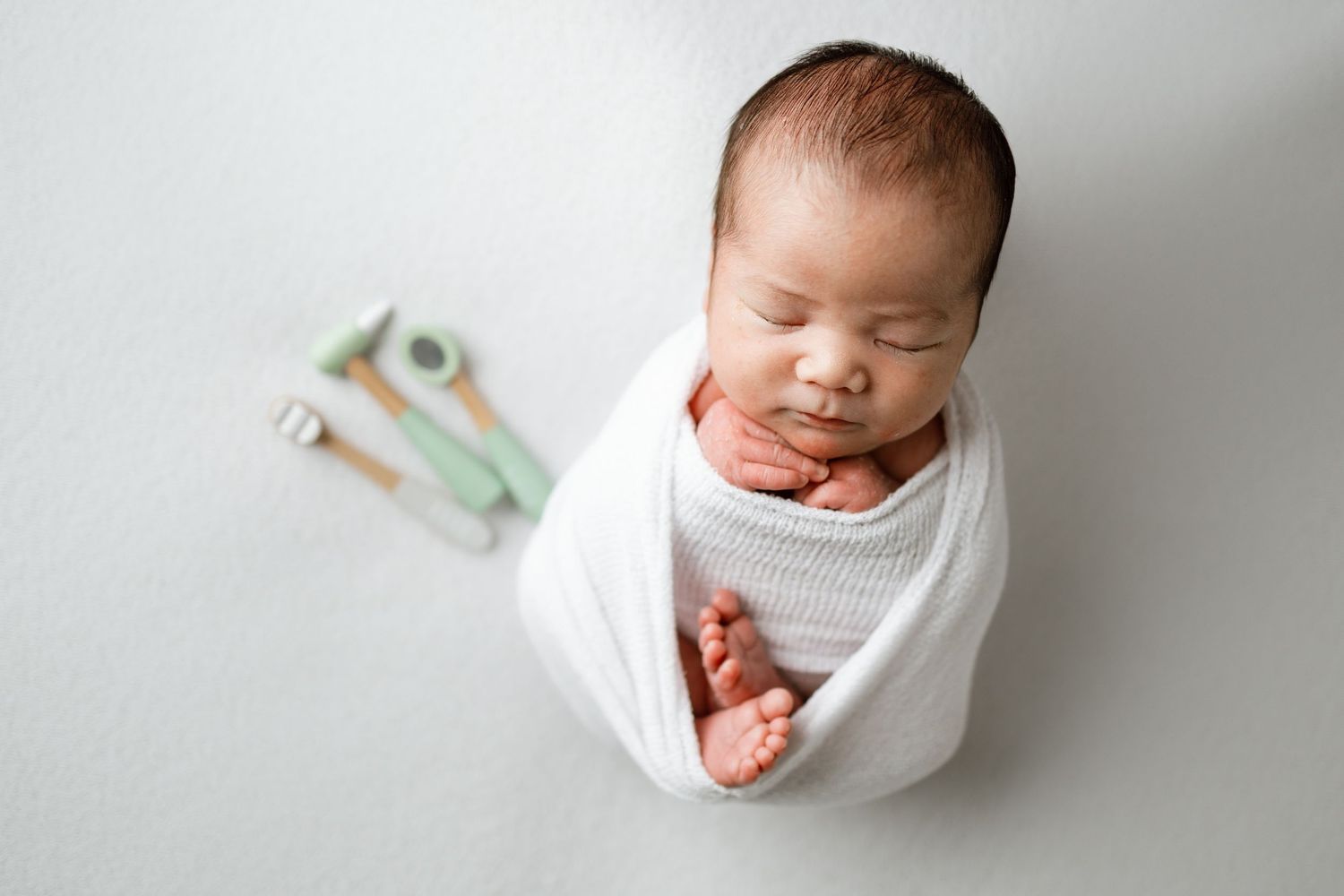 Peaceful sleeping newborn swaddled in soft white fabric against neutral backdrop.
