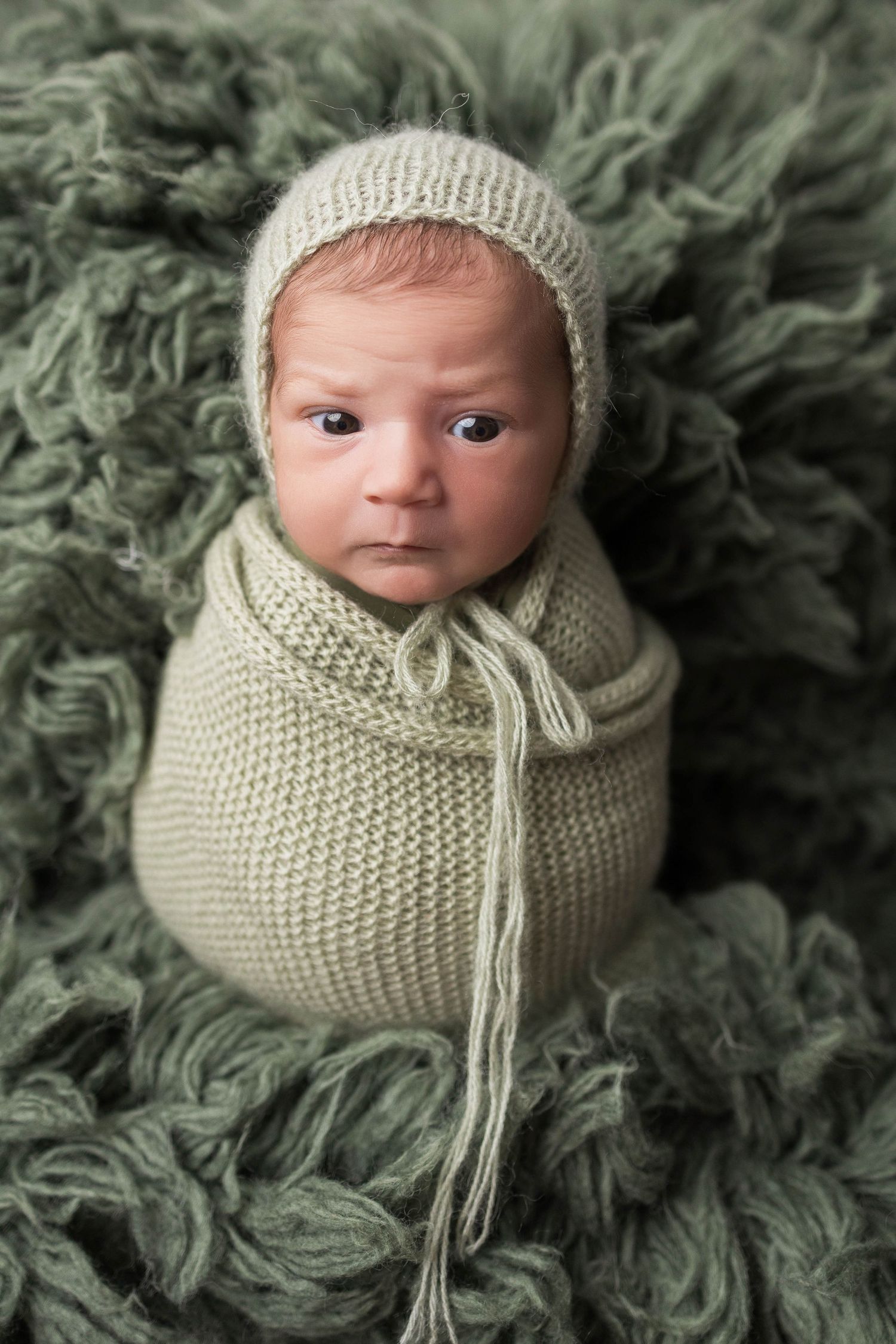 Close up photos of a newborn baby wrapped in a cream knit wrap against a green textured fur blanket background.
