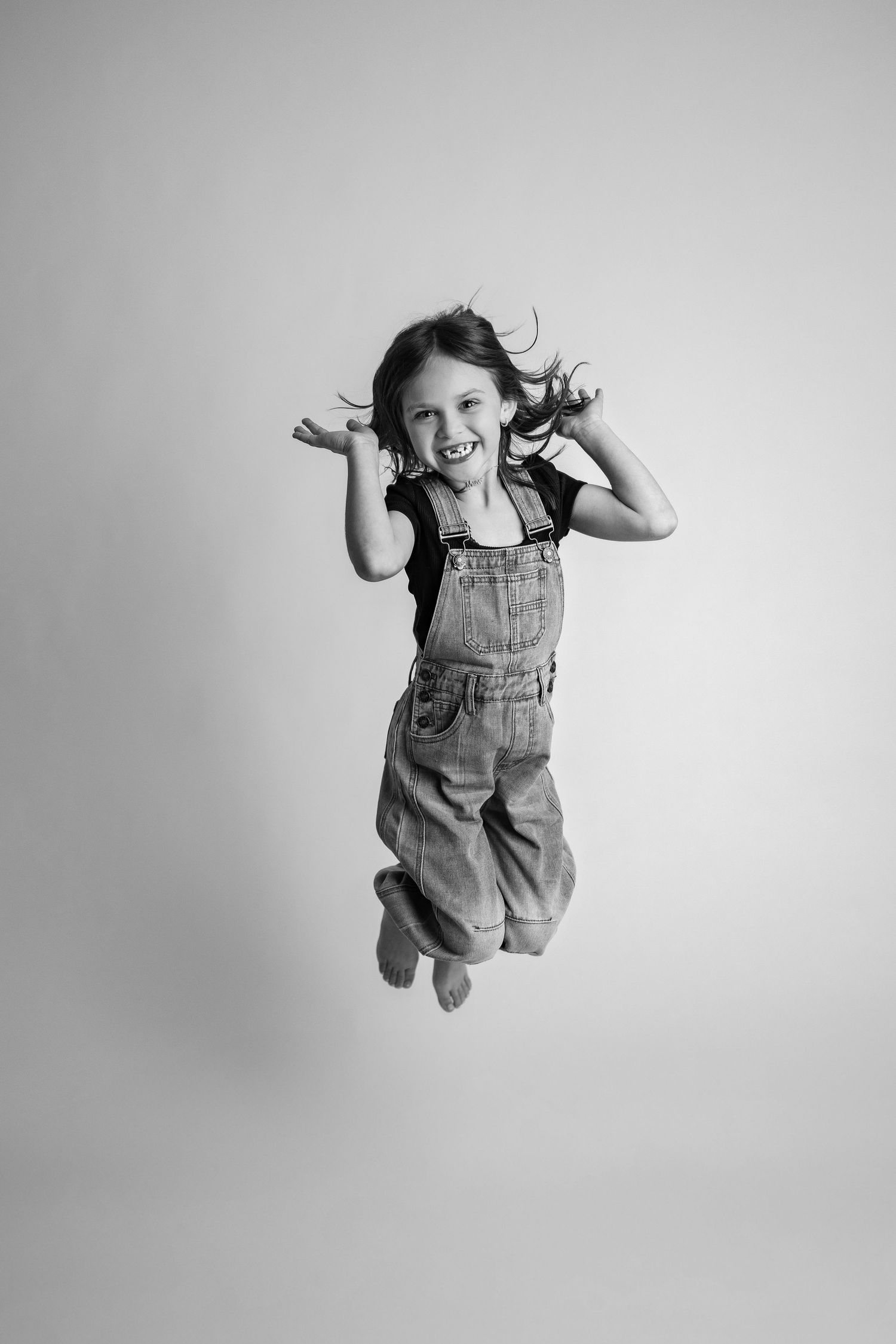 Black and white sequence showing a small child in overalls jumping and playing with joyful energy against a plain backdrop.