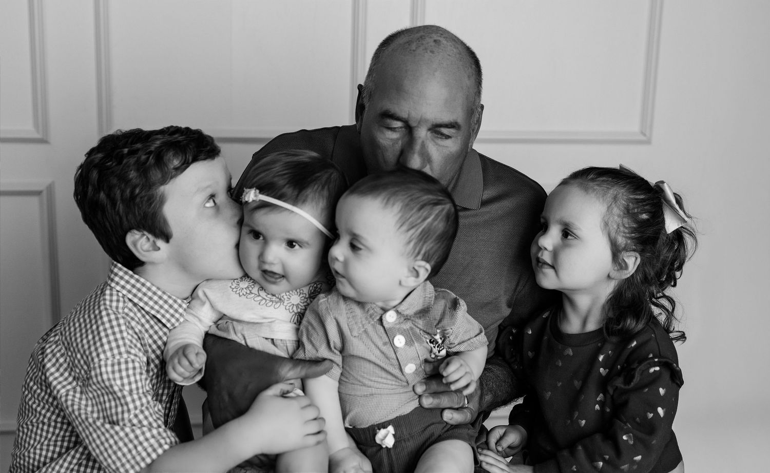 Black-and-white portrait of a grandfather cuddling his four grandchildren during a multigenerational studio session