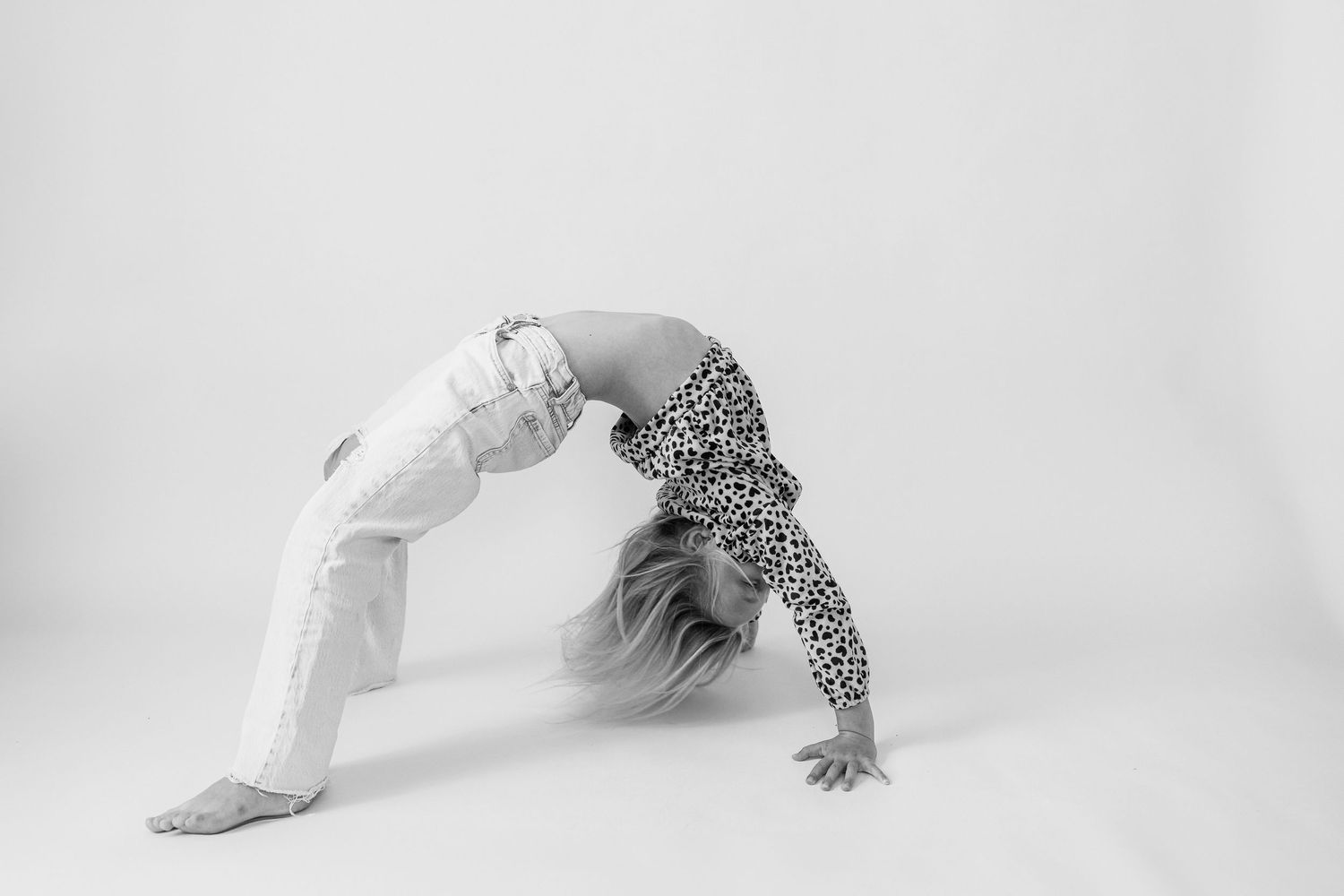 Dancer in white pants and patterned top performs a graceful backbend pose against a stark white background.