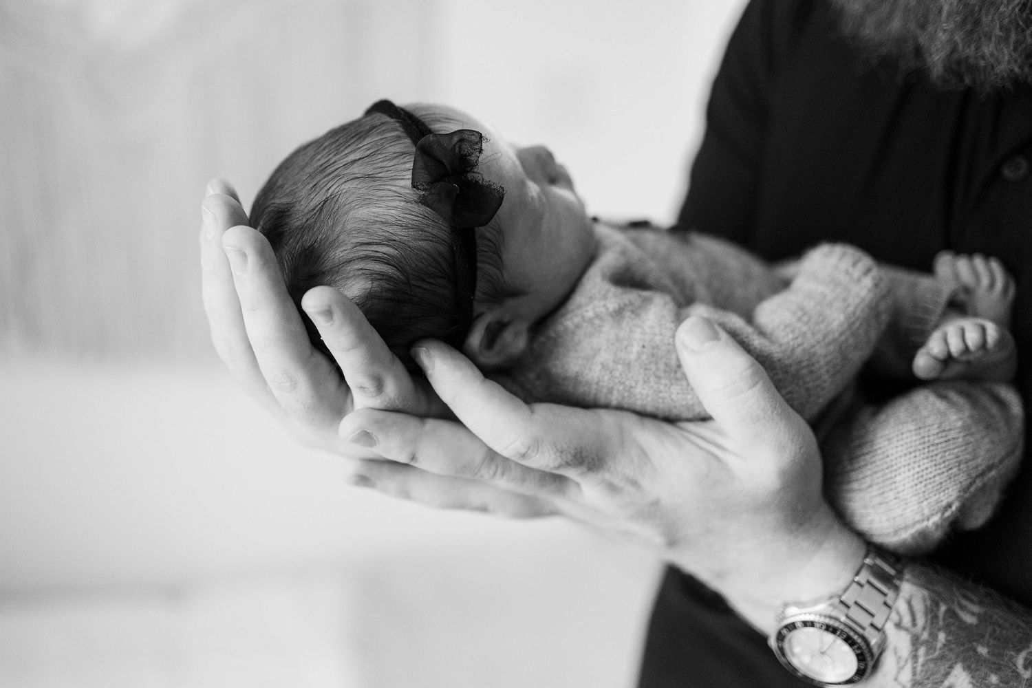 Black and white photo of tiny newborn baby gently held in adult hands showing delicate nurturing moment.